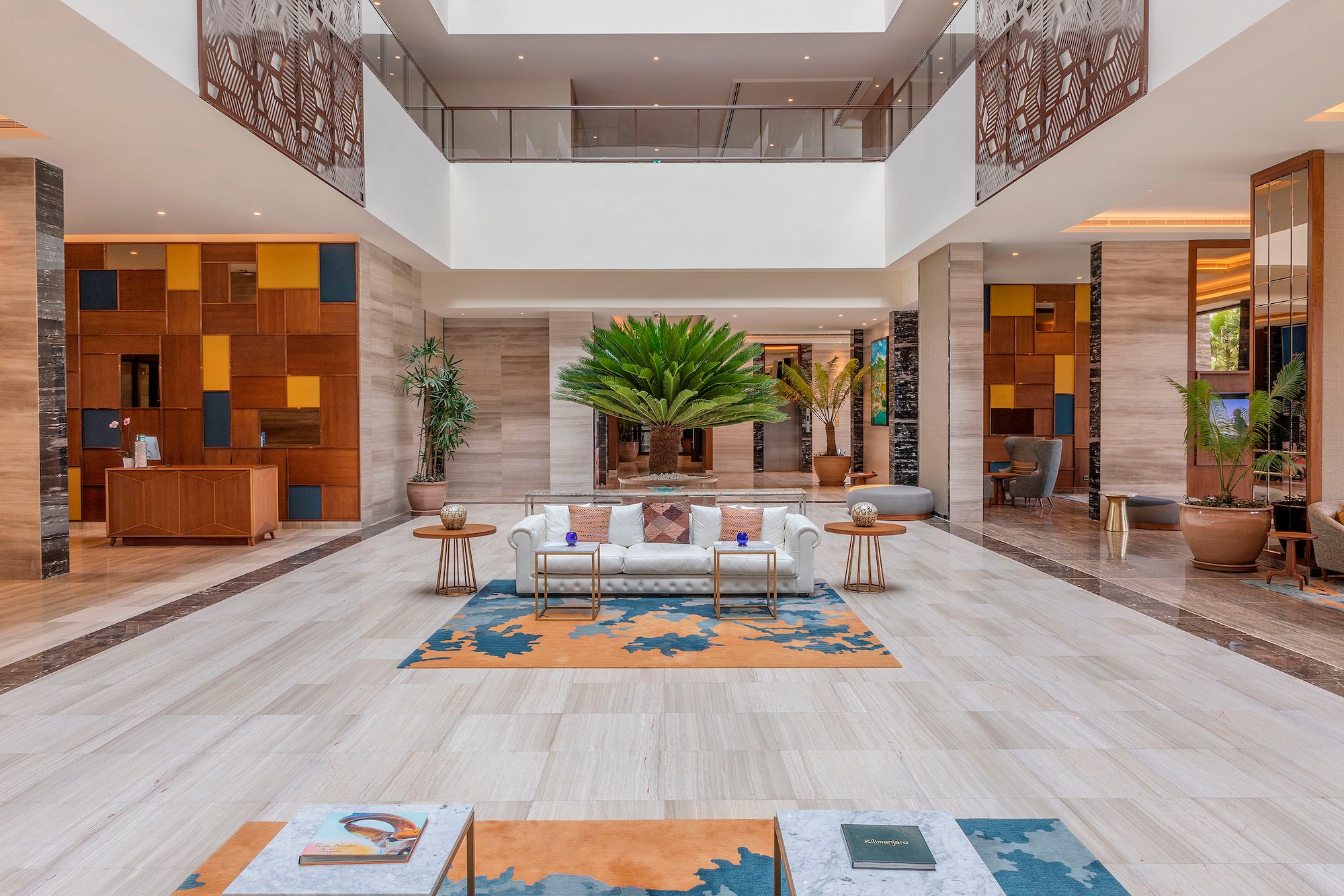 Spacious hotel lobby with modern design, large palm tree, white sofa, marble floors.