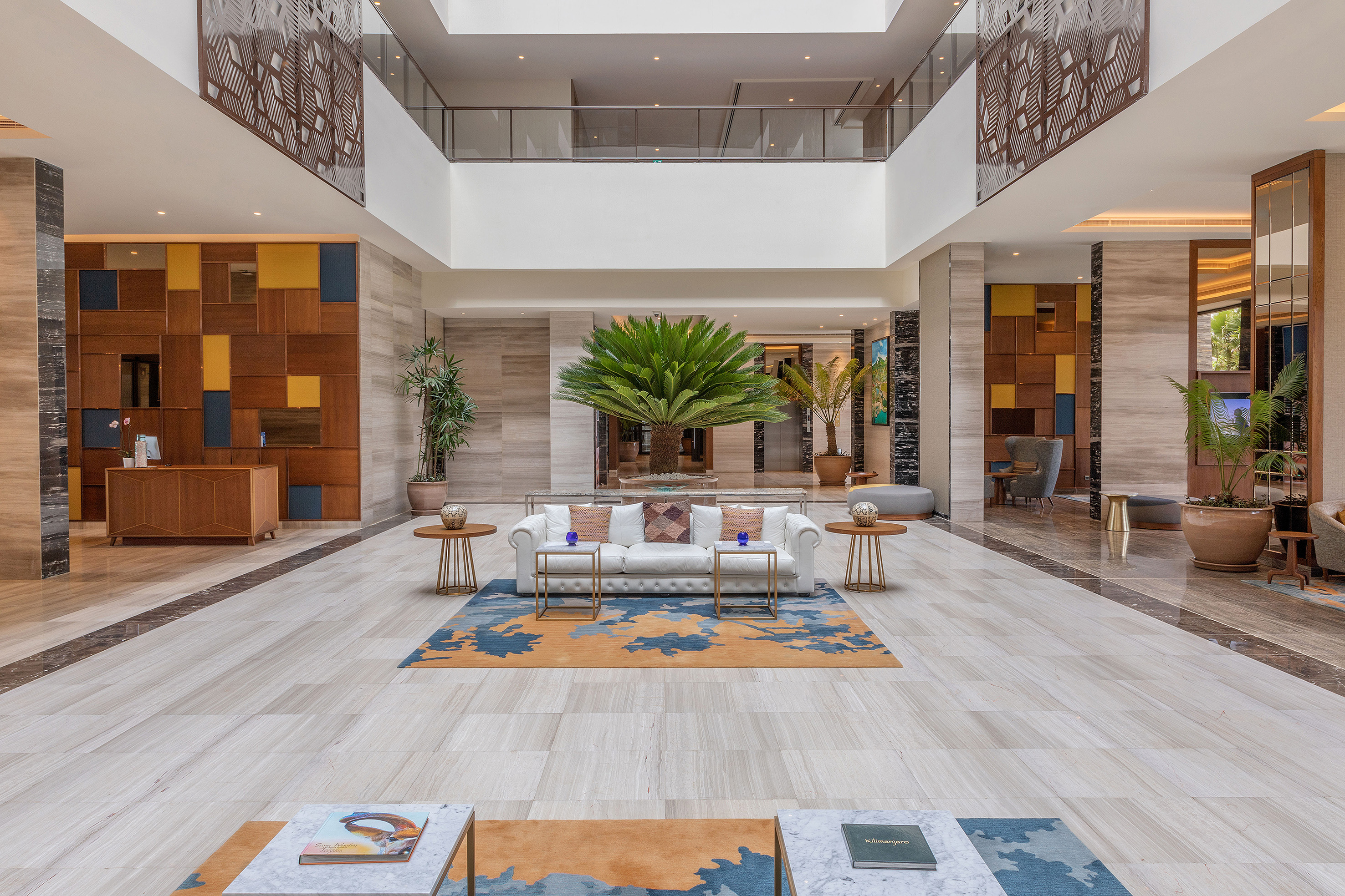 Spacious hotel lobby with modern design, large palm tree, white sofa, marble floors.