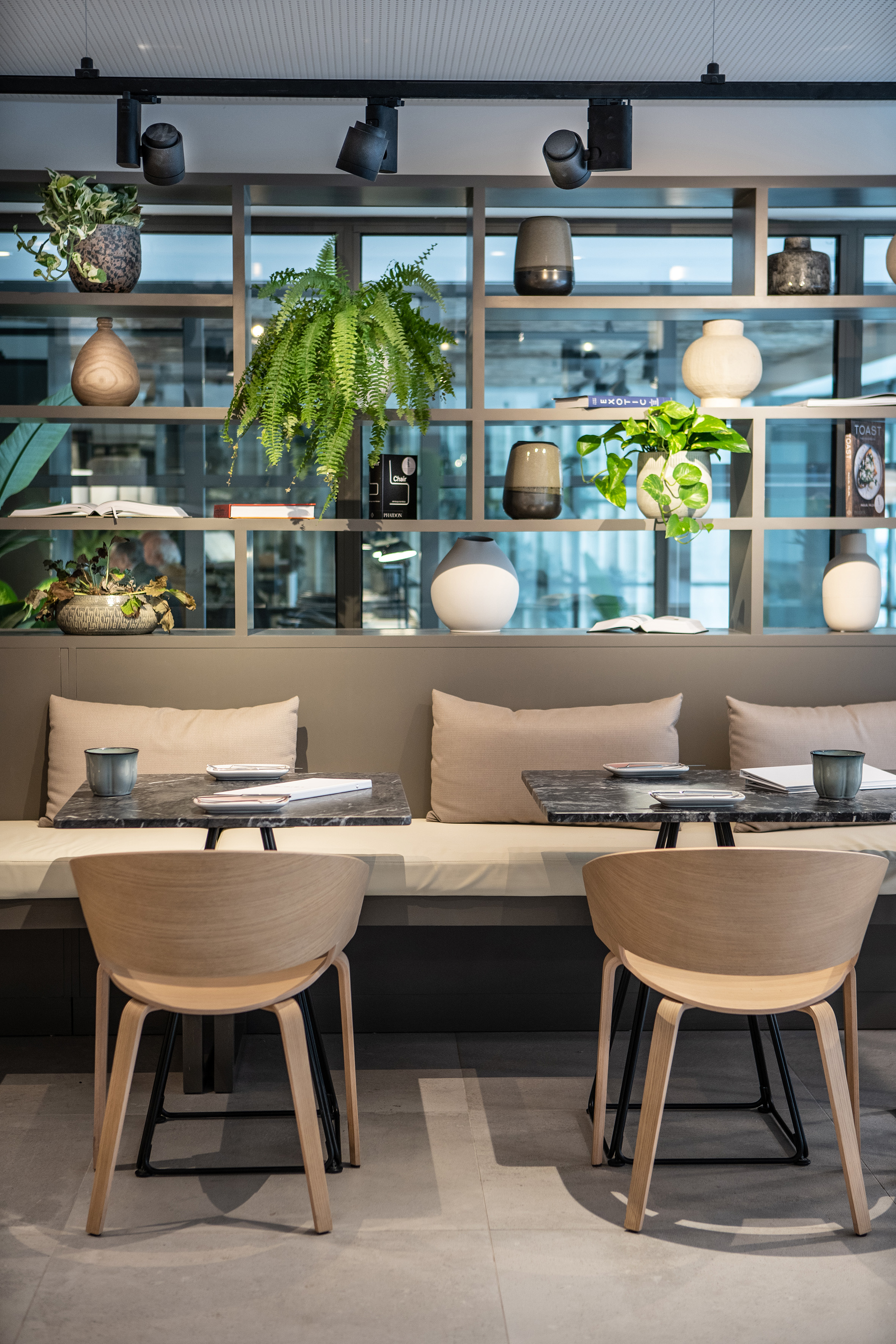 Modern cafe interior with dining tables, chairs, and plant-decorated shelves.