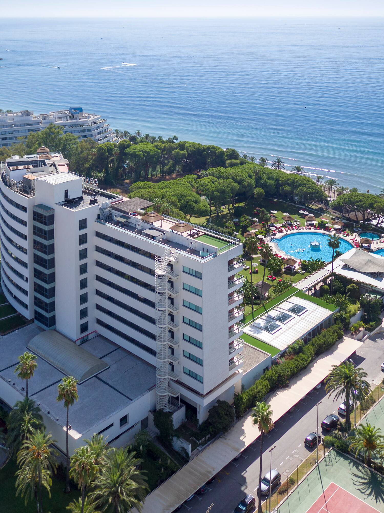 a large white building with a swimming pool and trees next to a body of water