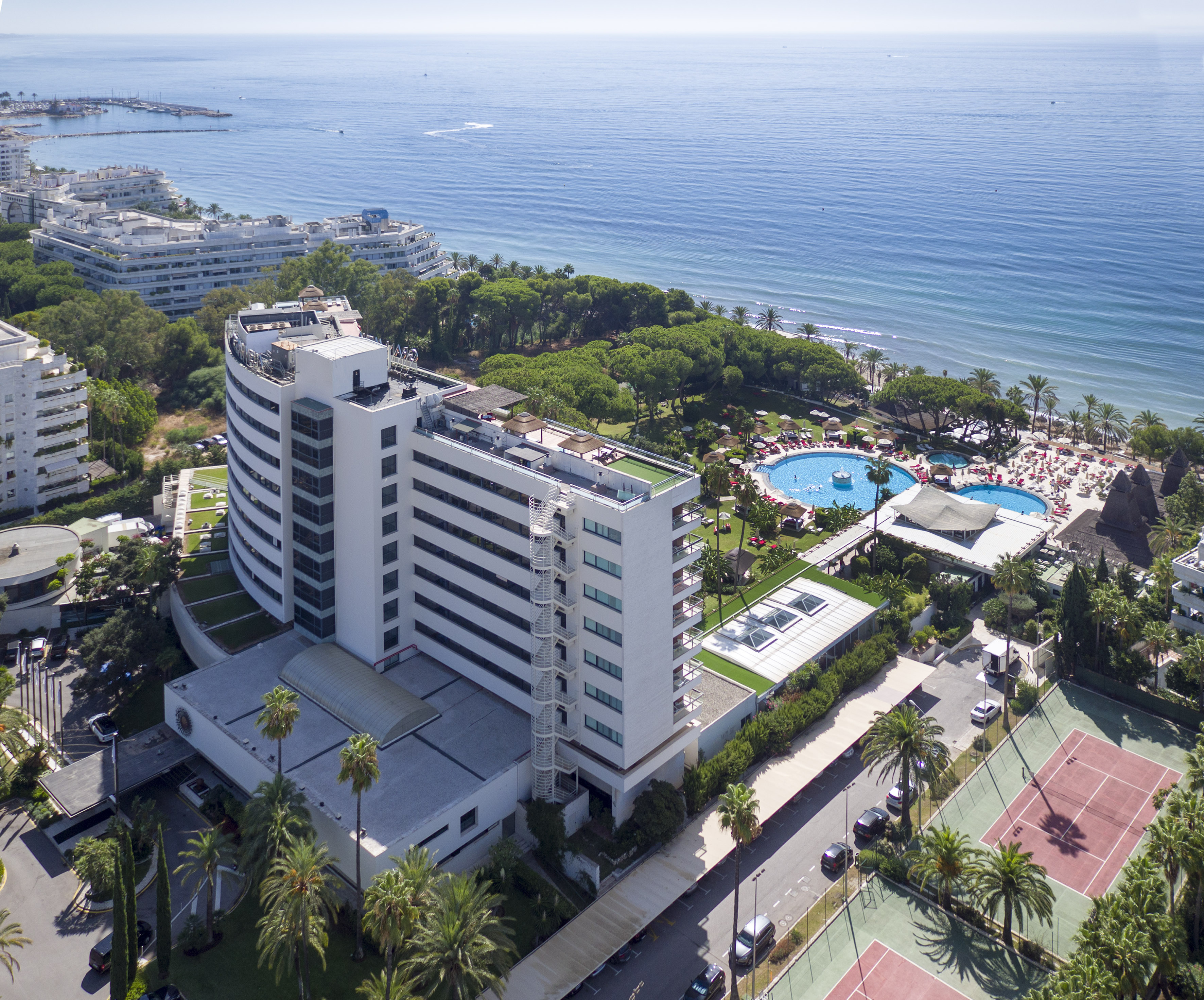 Luxury beachfront hotel aerial view: ocean, pools, palm trees, tennis courts.