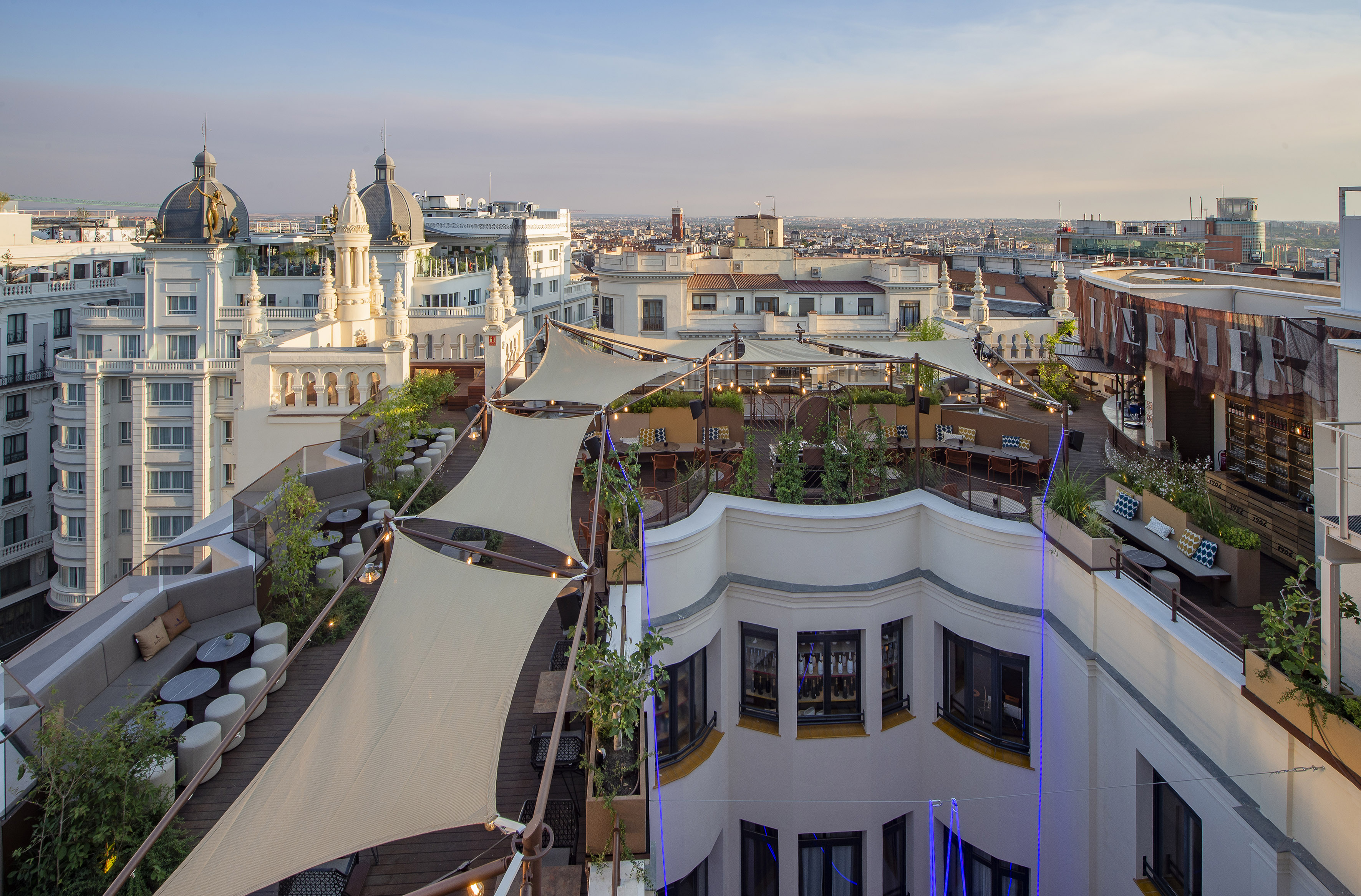 Madrid rooftop terrace bar with white canopies, outdoor seating, and city view.