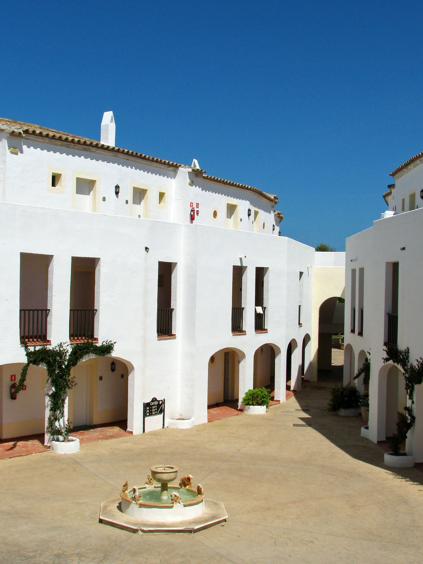 White Mediterranean courtyard, arched entrances, fountain, blue sky.