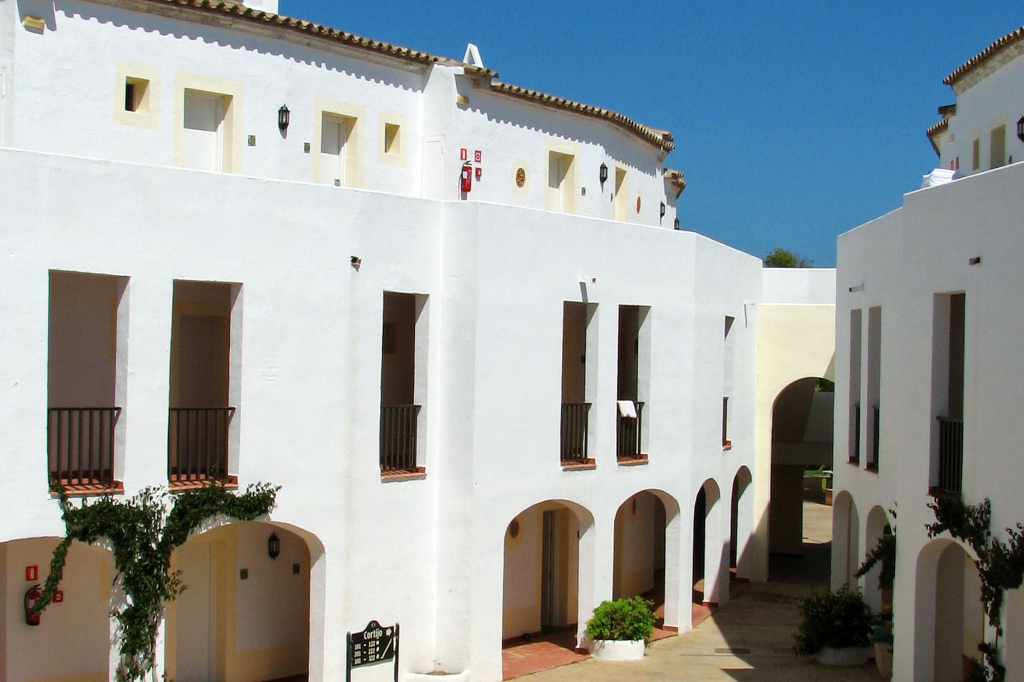White Mediterranean courtyard, arched entrances, fountain, blue sky.