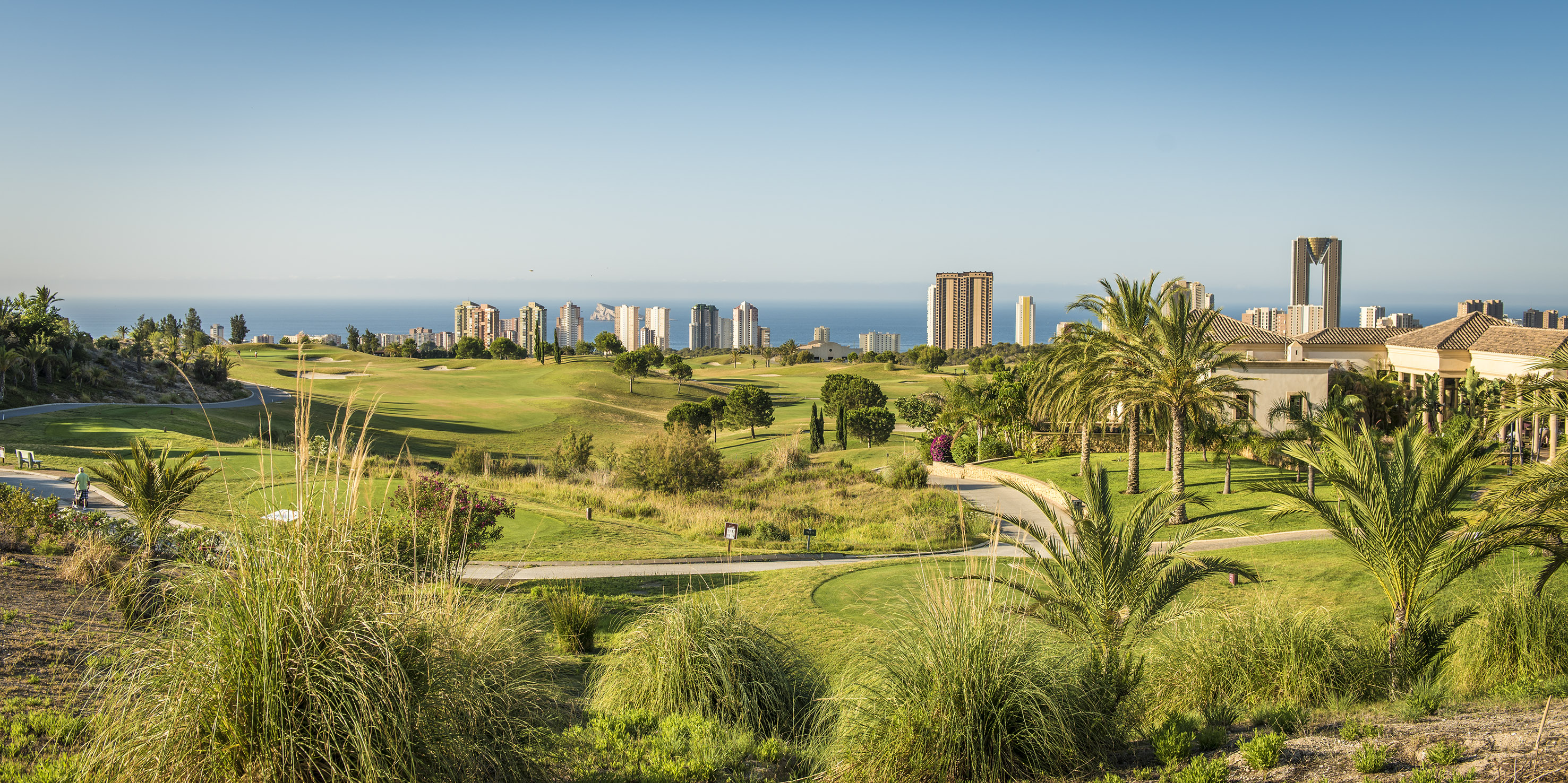 Golf resort with lush green course, ocean view, and distant city skyline.