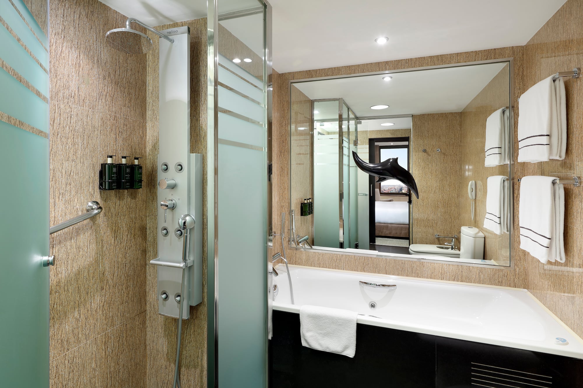 Baño de hotel moderno con ducha de hidromasaje, bañera y toallas blancas.