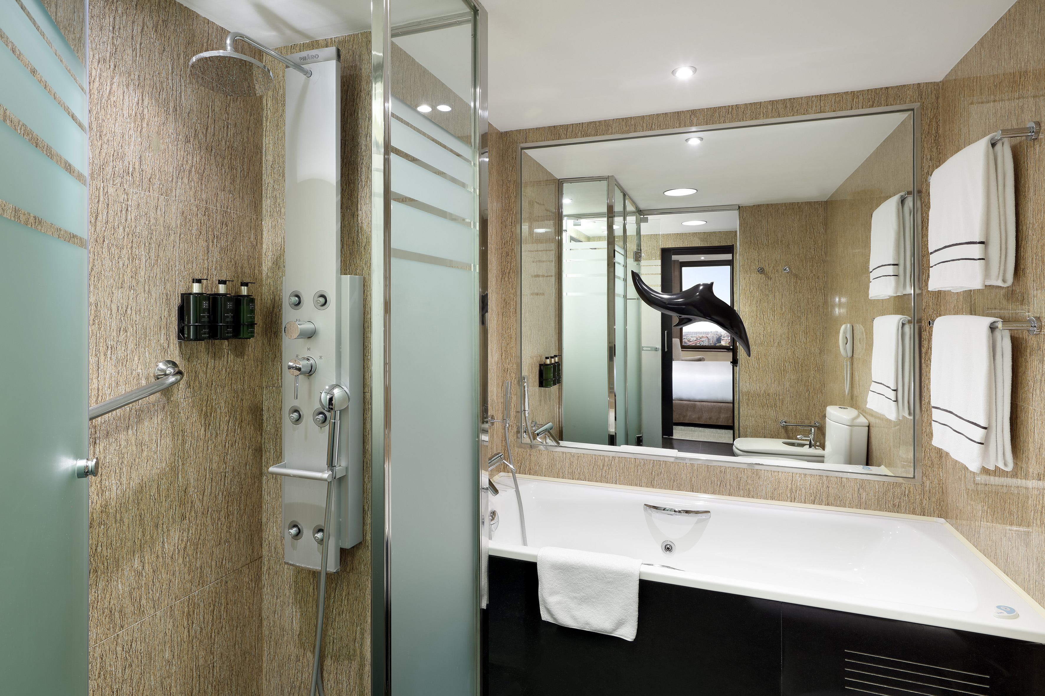Baño de hotel moderno con ducha de hidromasaje, bañera y toallas blancas.