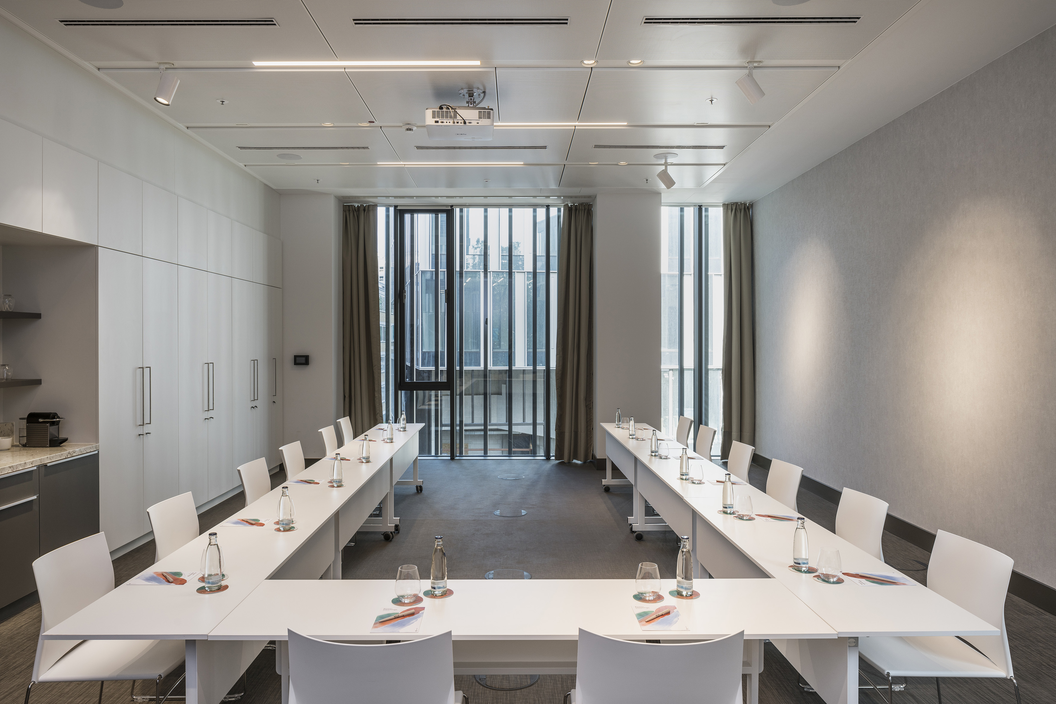 Bright modern conference room with U-shaped tables, white chairs, and projector.