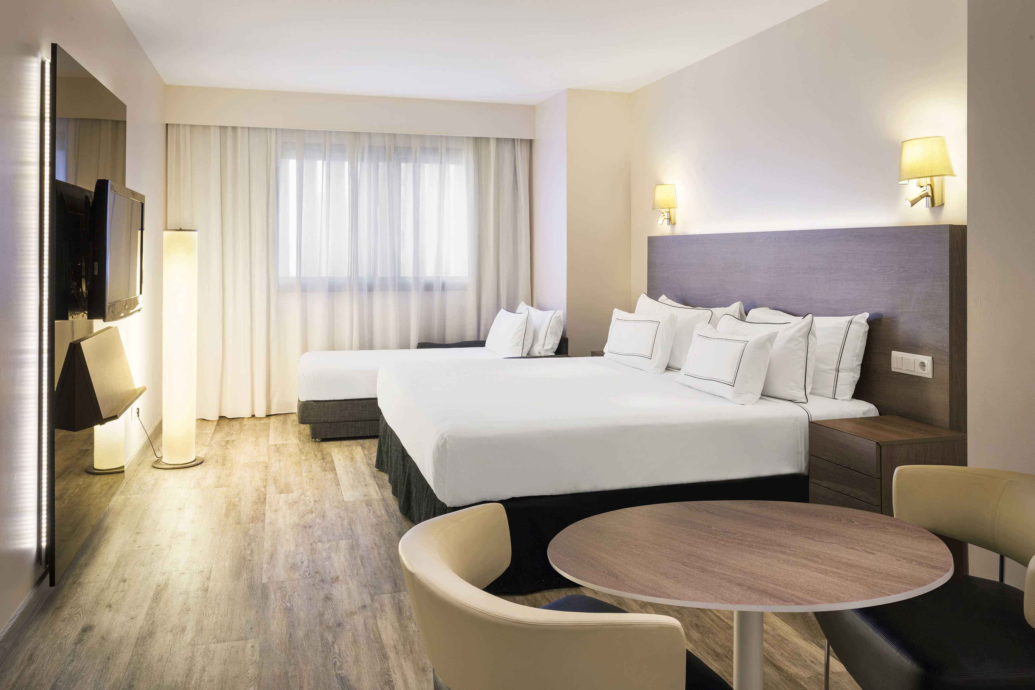 Modern hotel room with king bed, sofa, table, TV, and window.