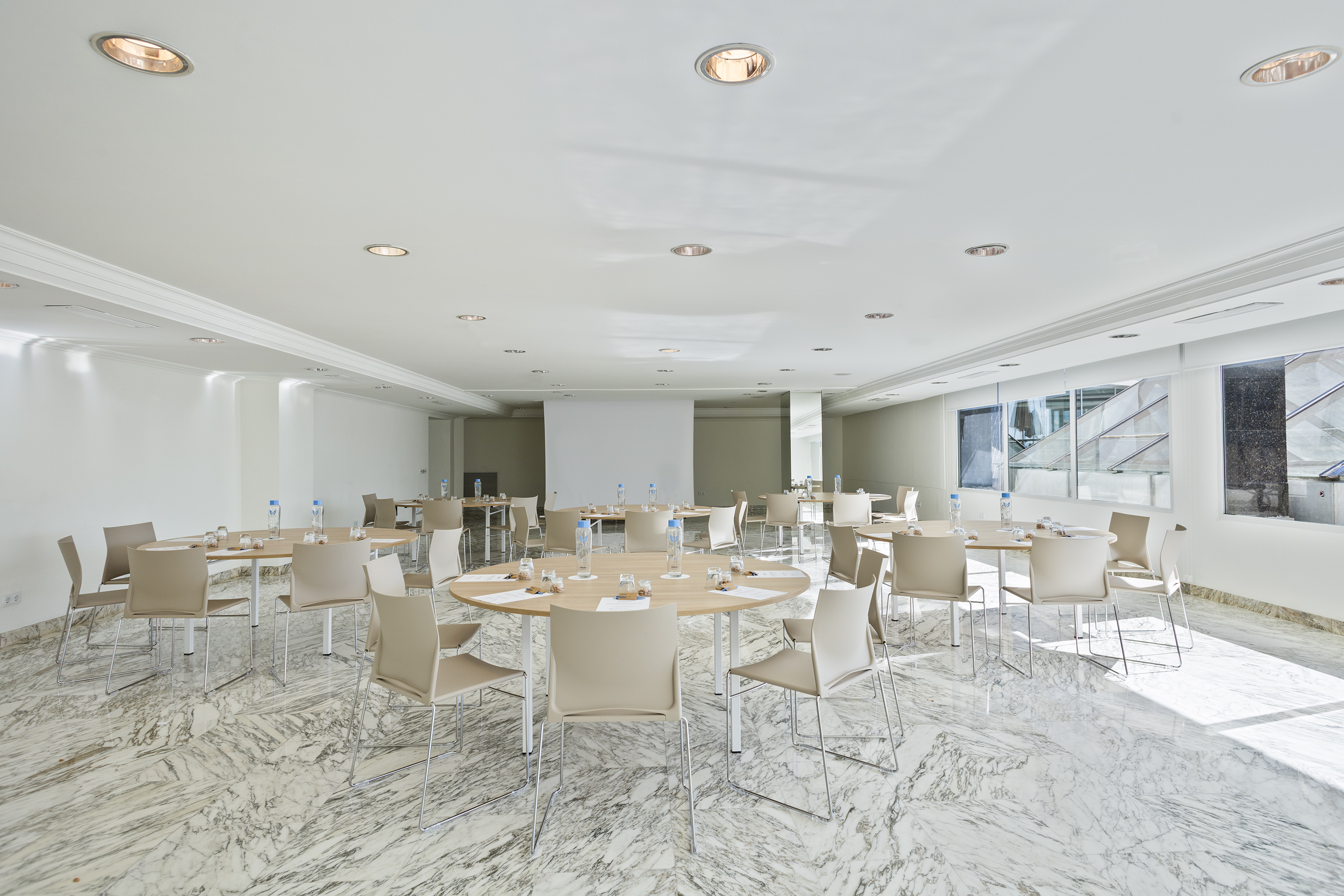 Modern meeting room with round tables, beige chairs, and marble floor.
