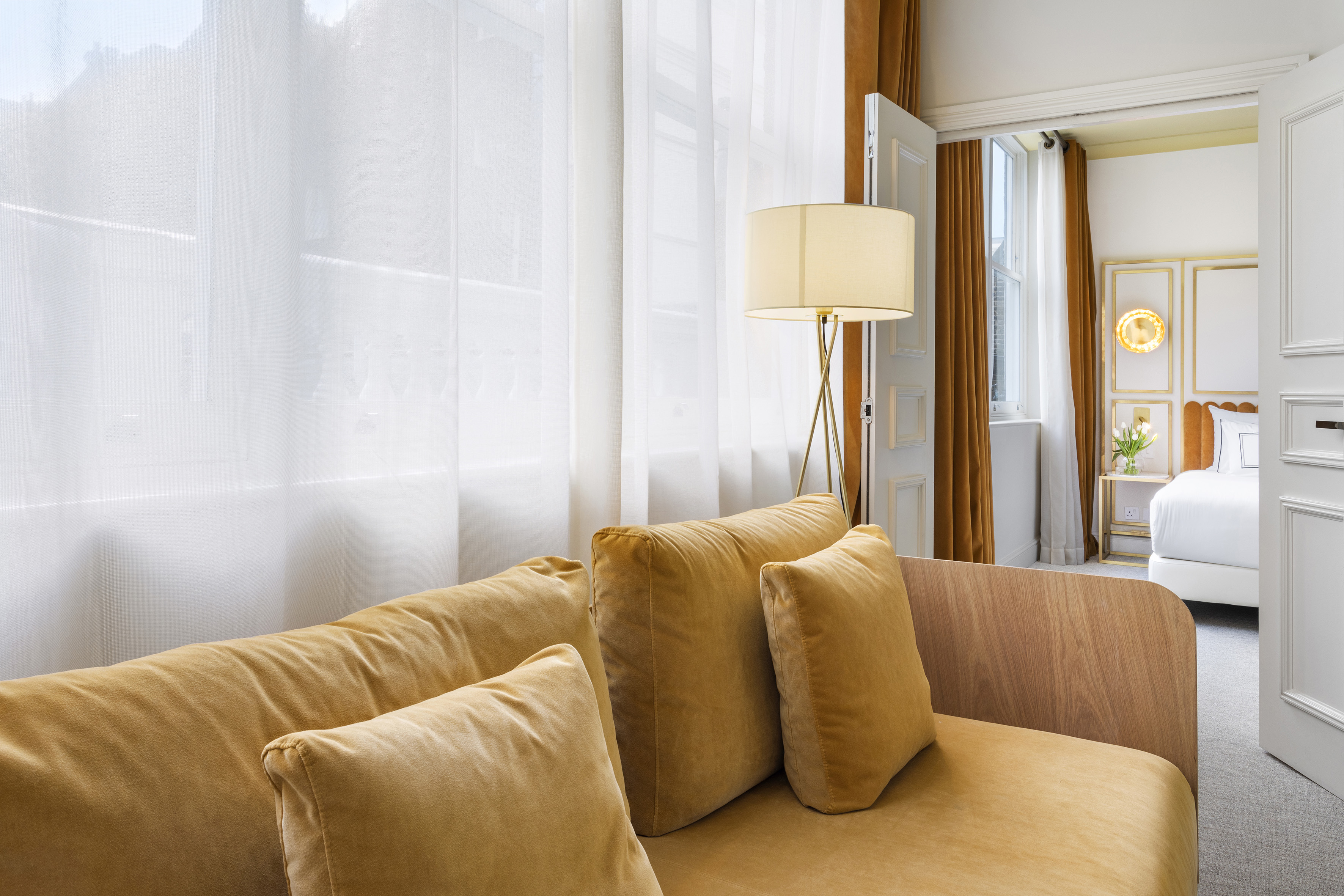 Golden velvet sofa in modern hotel suite living area, bedroom visible.