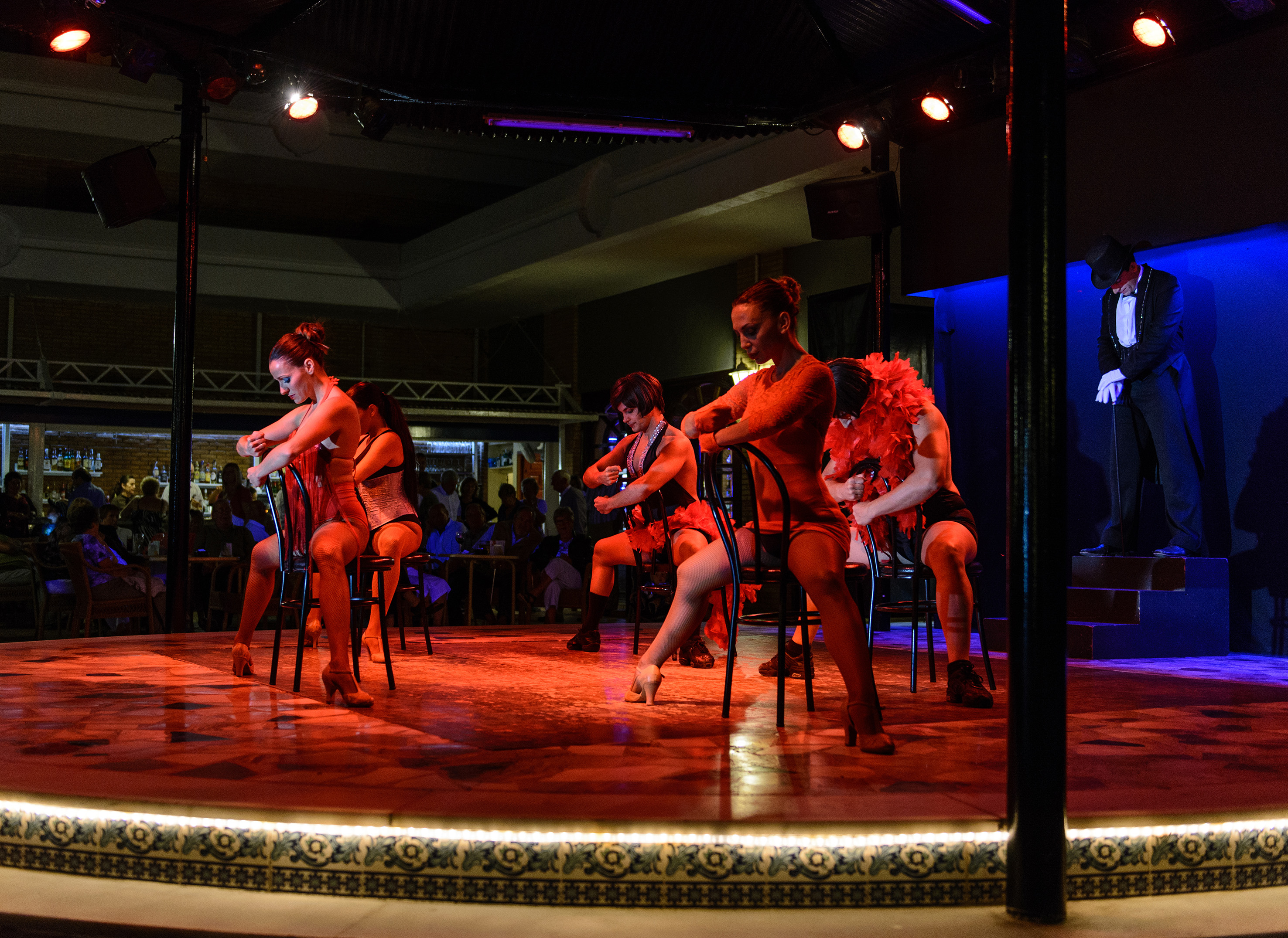 Cabaret dancers in red on a red-lit stage with a tuxedoed showman.