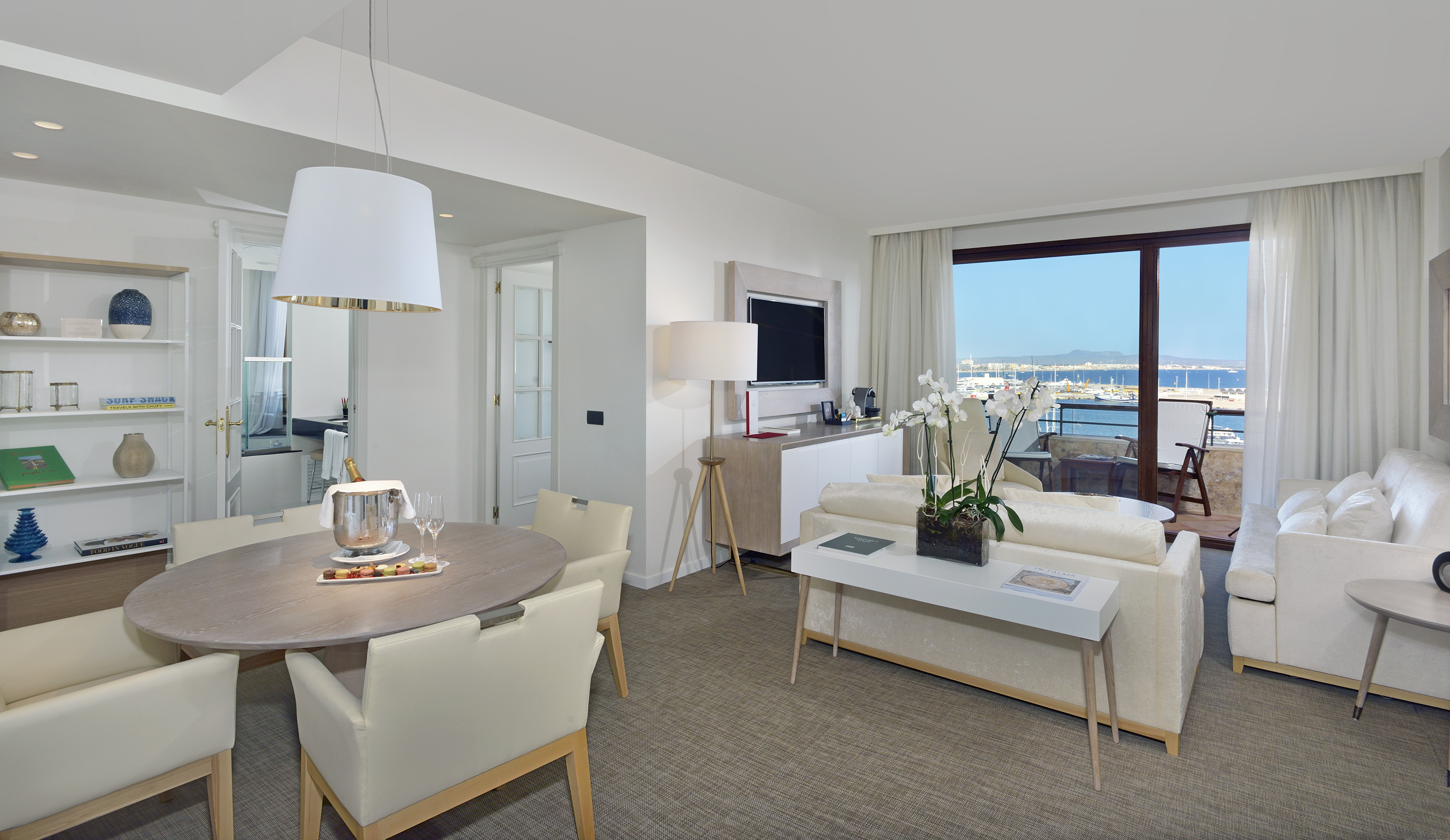 Luxury hotel suite with modern living and dining areas, waterfront marina view.