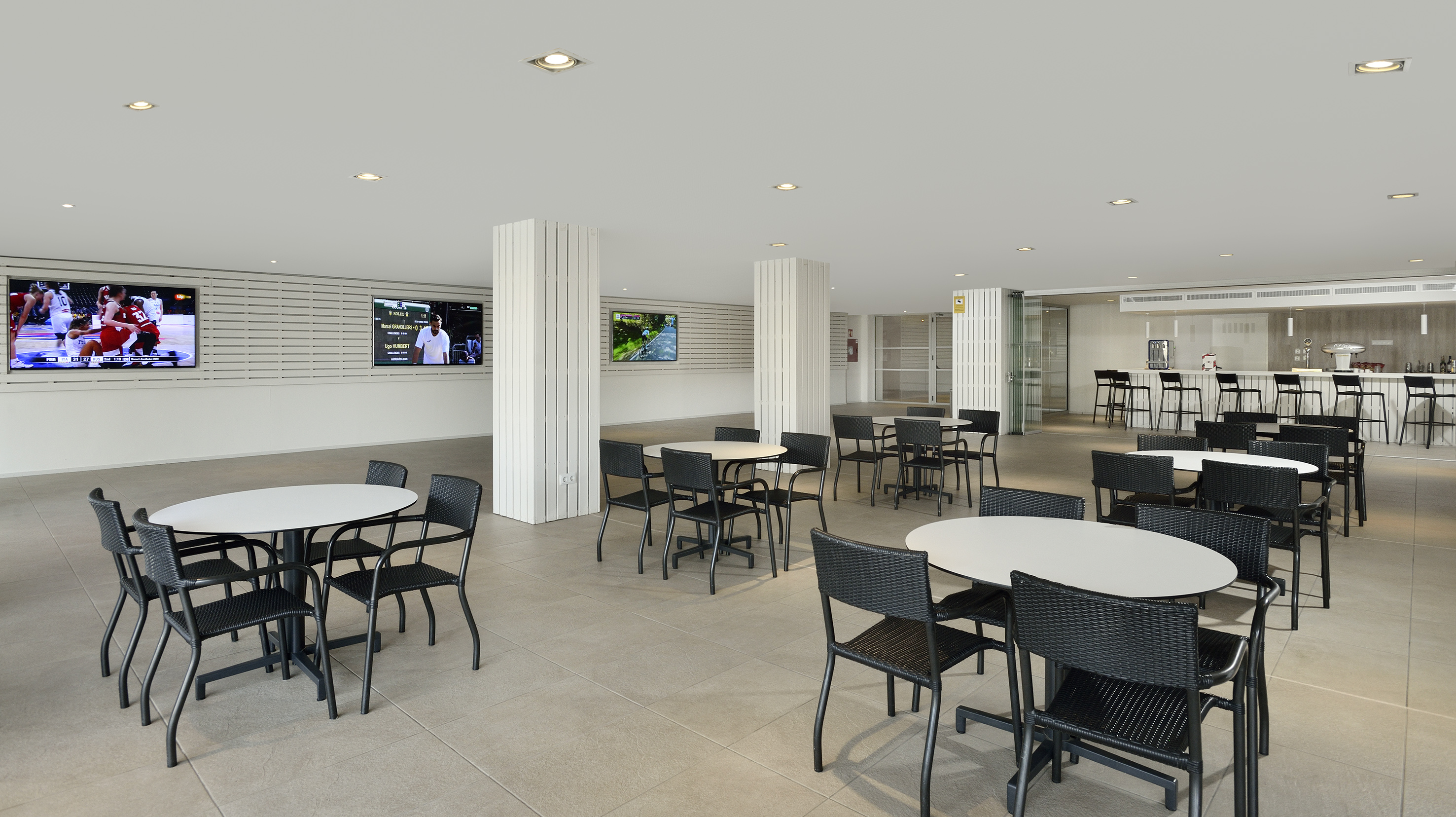 Contemporary dining area with black tables, chairs, bar, and sports screens.