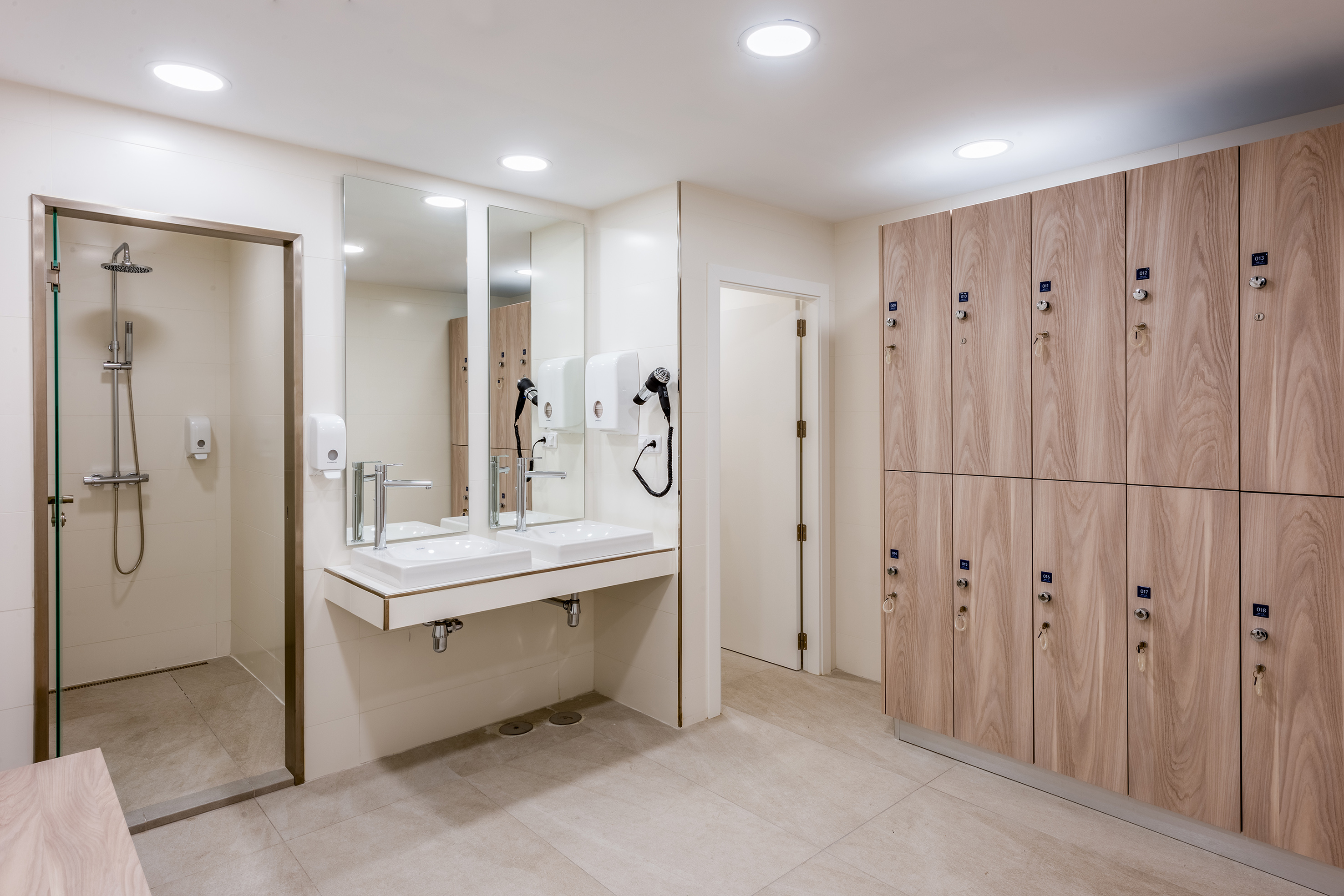 Modern gym locker room with showers, dual sinks, and wooden lockers.