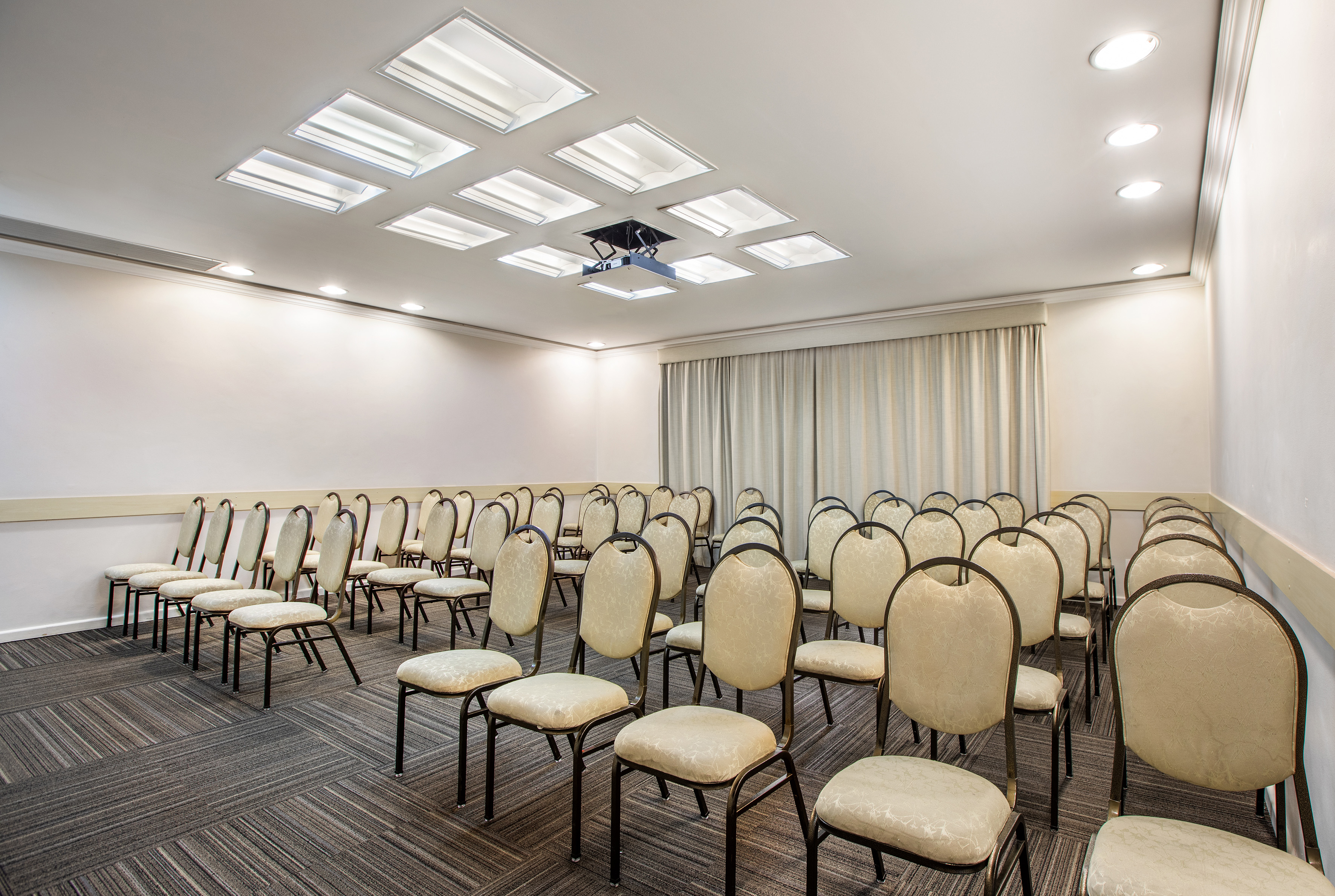 Empty meeting room with light chairs, ceiling projector, and patterned carpet.