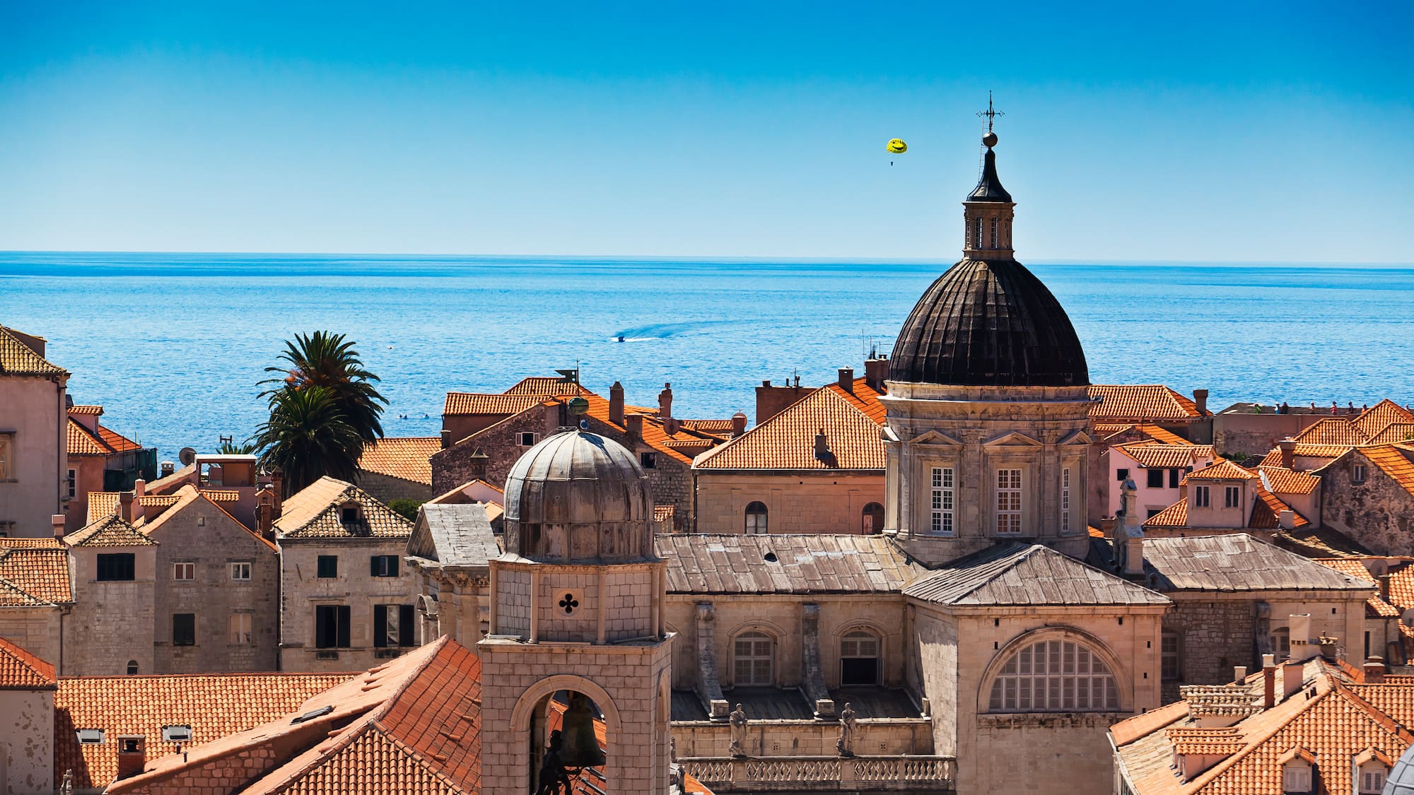 a rooftops of a town with a bell tower and a large body of water