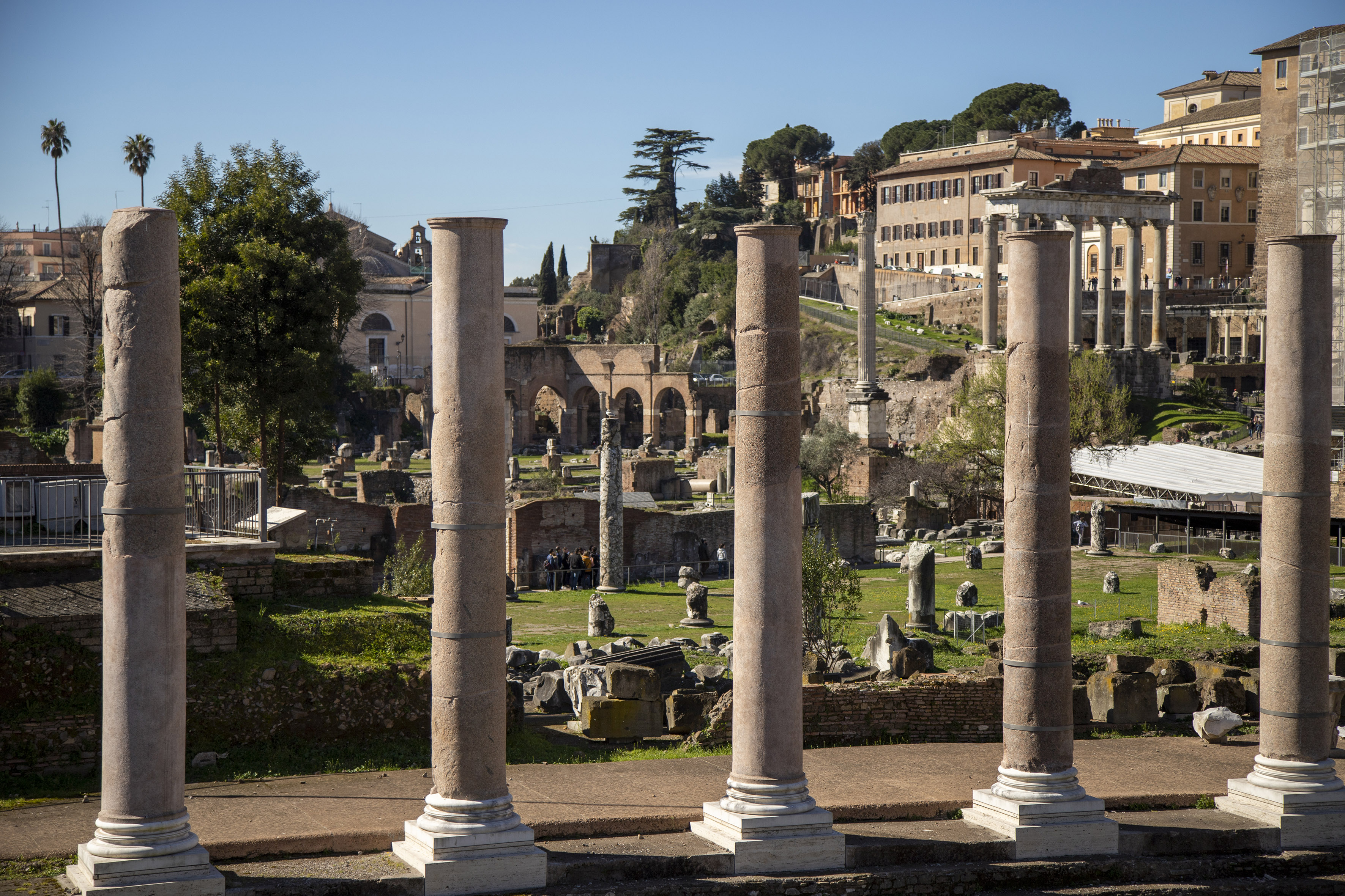a group of pillars in a grassy area with buildings in the background