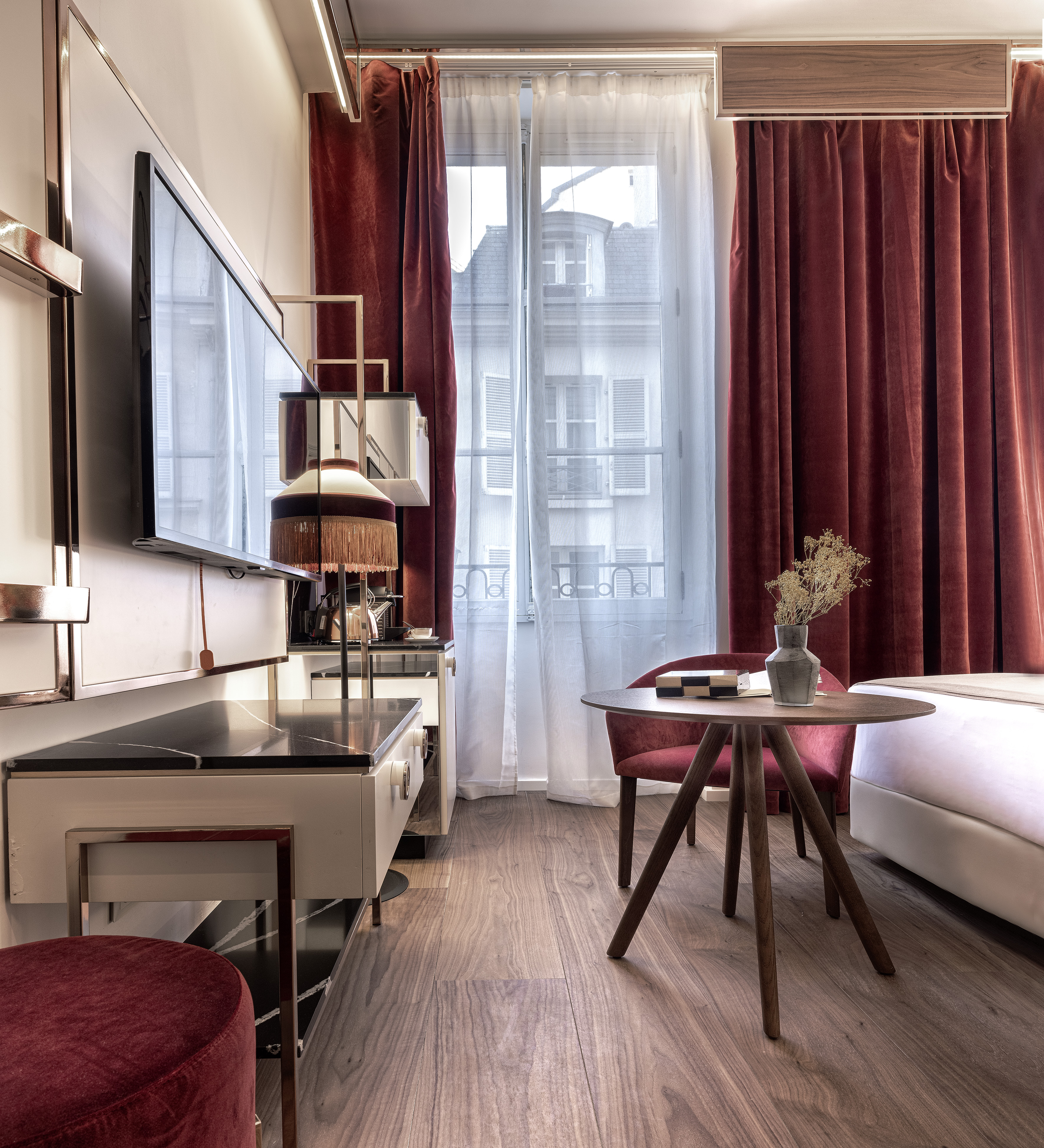 Elegant hotel room with red velvet accents, modern TV, and hardwood floor.