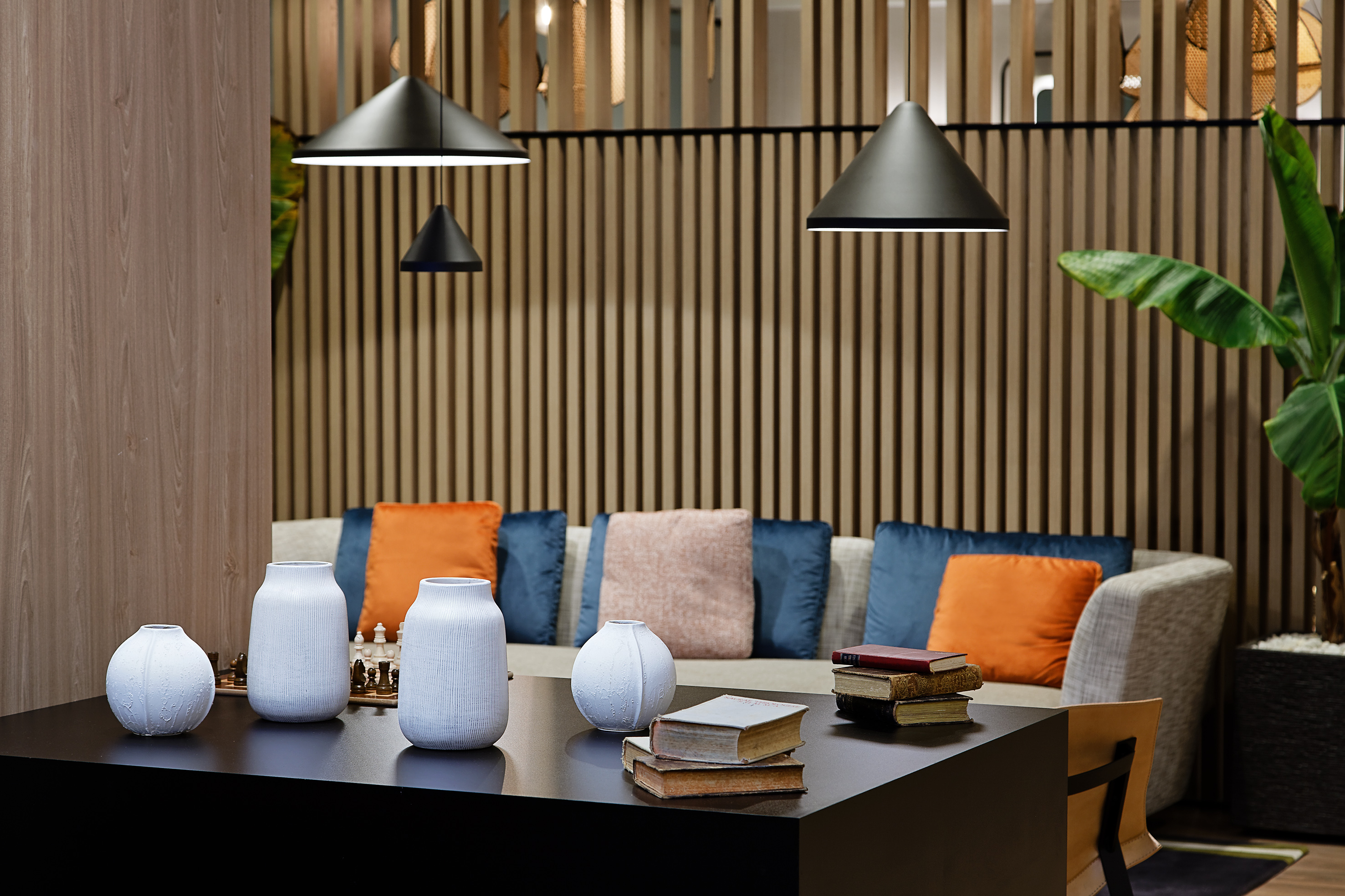 Modern lounge with black coffee table, sofa, wooden slat wall, and pendant lights.