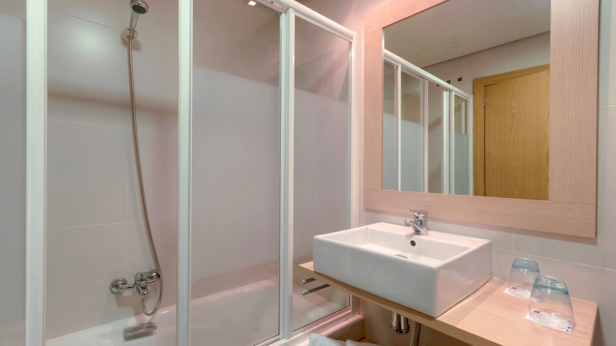 Modern hotel bathroom with shower, bathtub, rectangular sink, and wooden mirror.