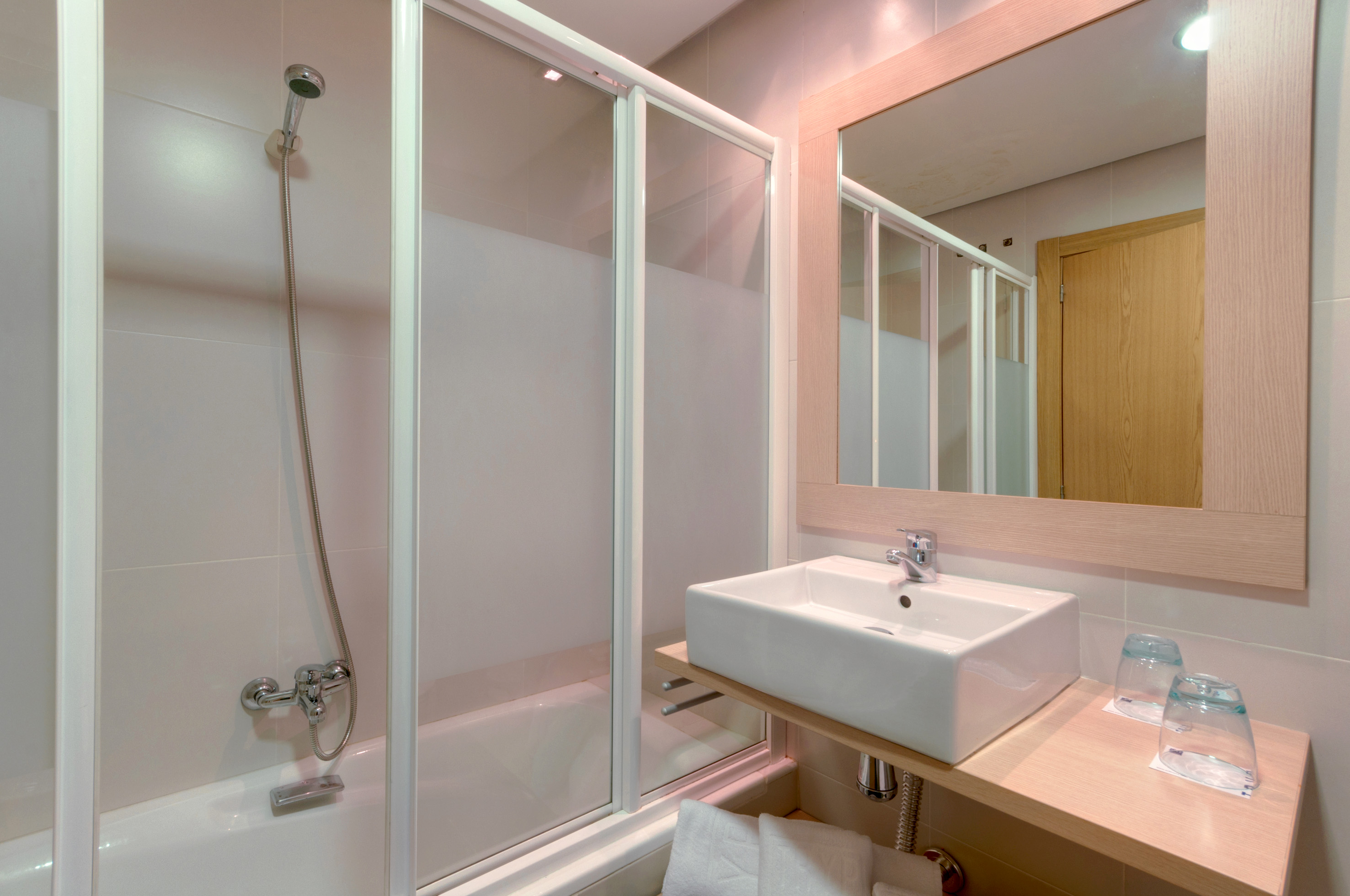 Hotel bathroom with bathtub, shower, modern sink, and large vanity mirror.