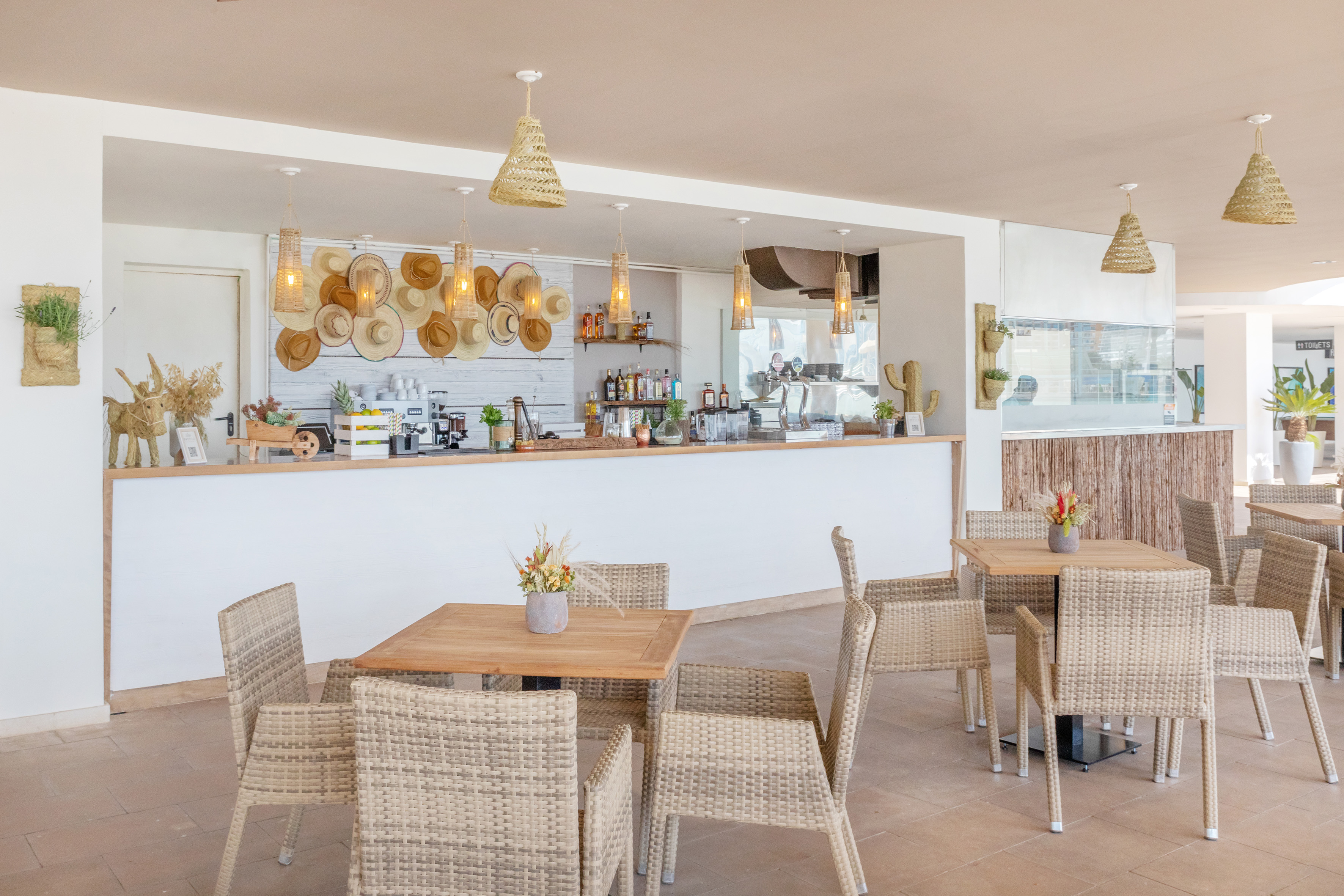 Bright hotel bar with wicker chairs, wooden tables, and straw hat decor.