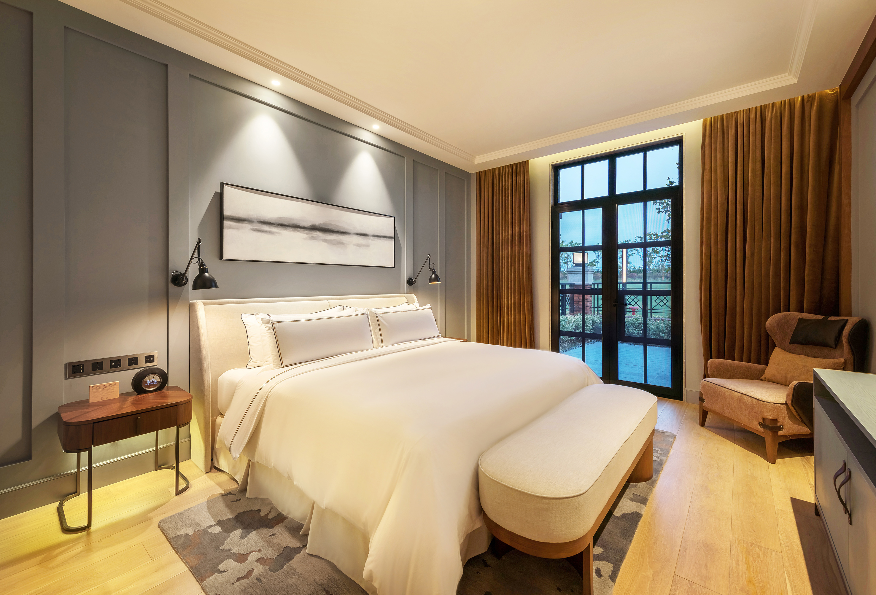 Modern hotel bedroom with king bed, grey walls, large window, and wooden floor.