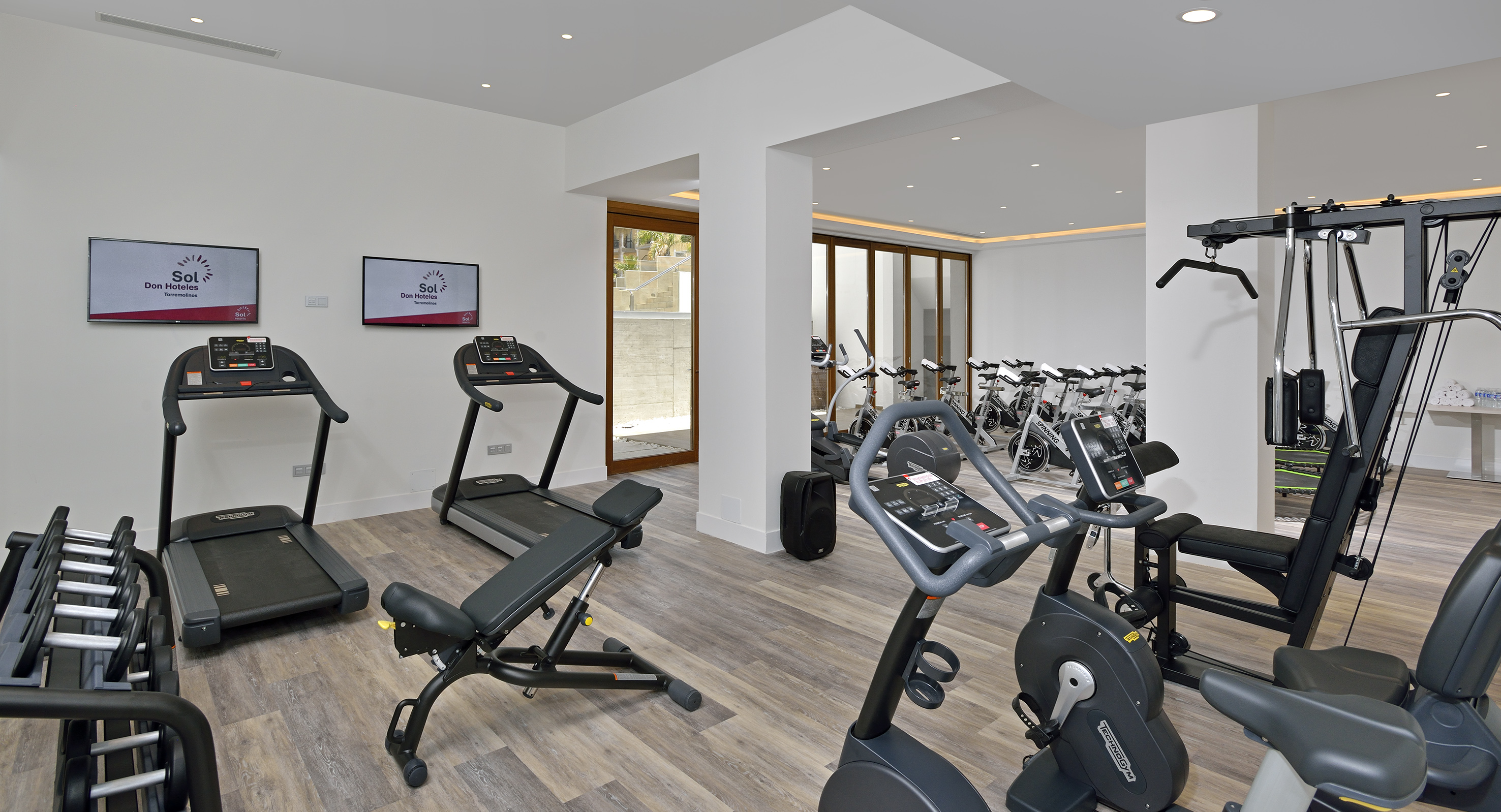 Modern hotel gym with treadmills, spin bikes, dumbbells, and weight machines.