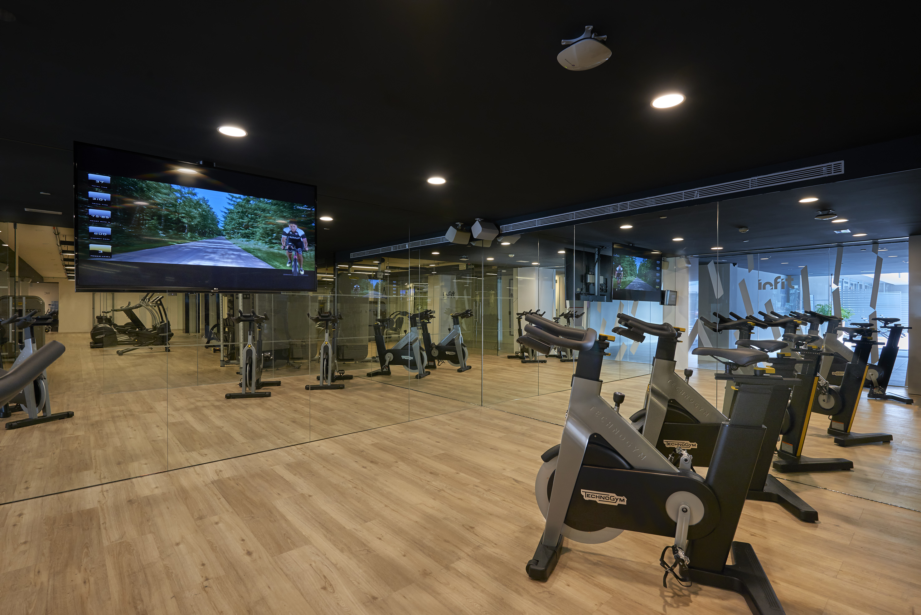 Technogym spin studio with bikes, large screen virtual cycling video, and mirrored walls.