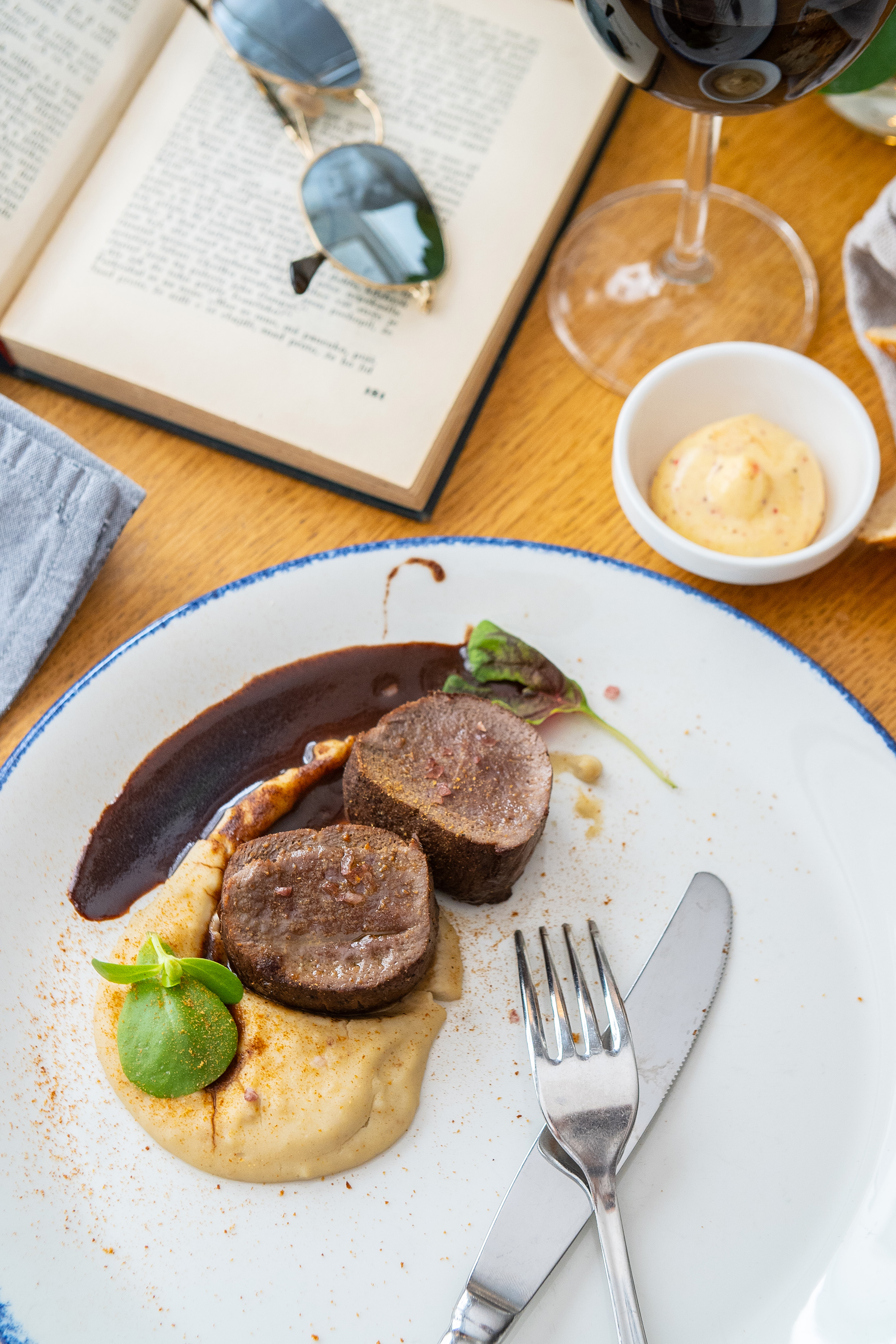 Gourmet beef medallions with rich sauce, puree, red wine, and an open book.