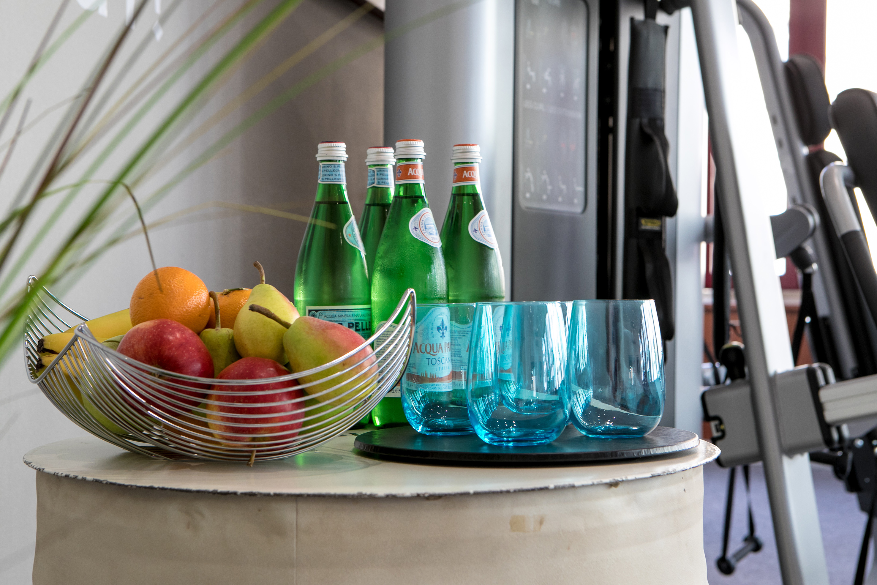 Fresh fruit bowl, sparkling water bottles, blue glasses in a fitness facility.