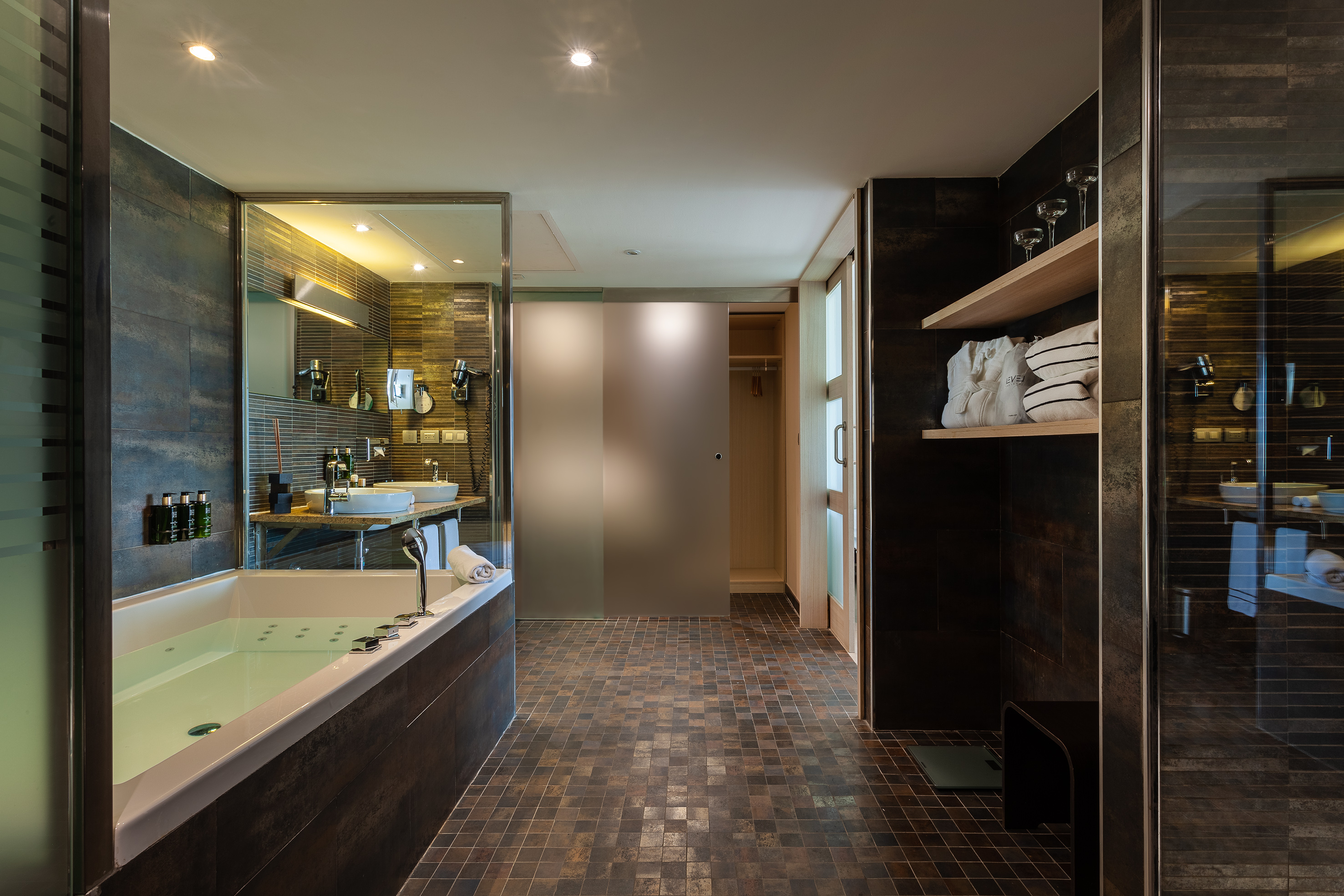 Modern hotel bathroom with jacuzzi, dual sinks, dark tile decor.