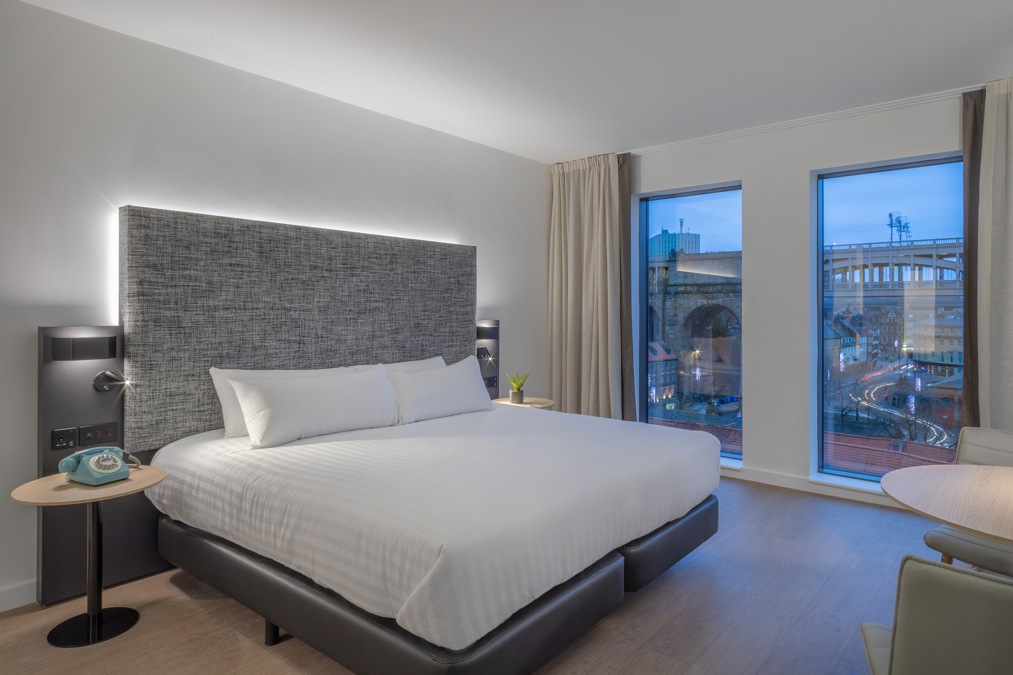 Modern hotel room with king bed, backlit headboard, and urban city view.