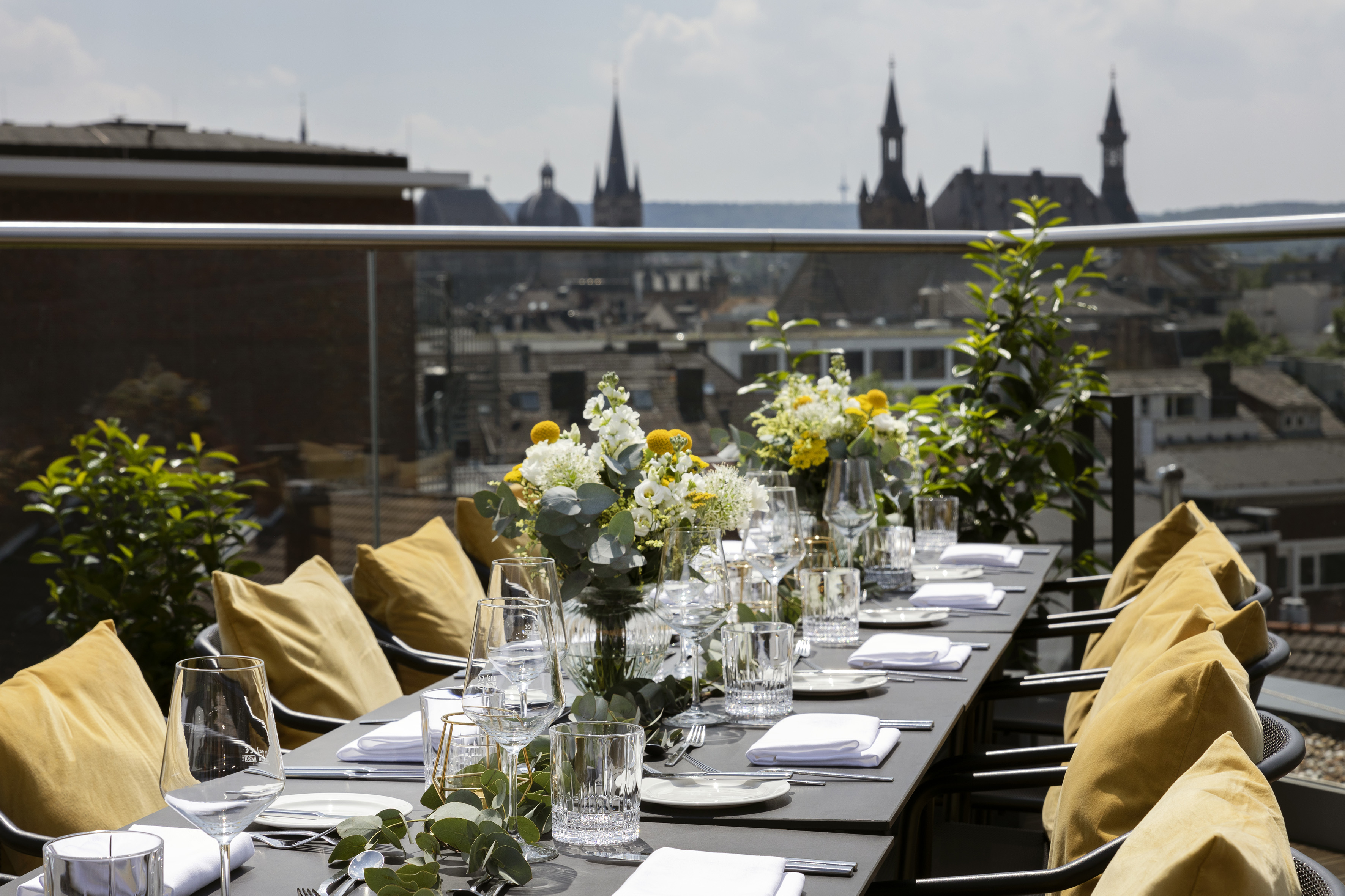 Rooftop terrace dining table set with yellow flowers and city skyline view.