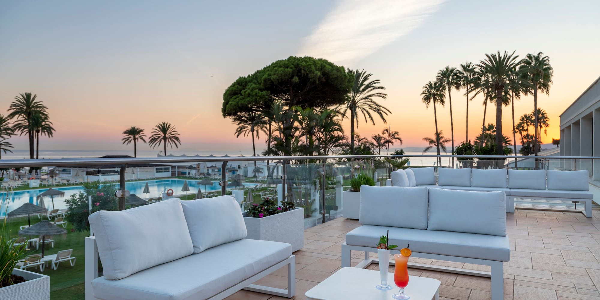 a white couches and tables on a patio with palm trees and a pool