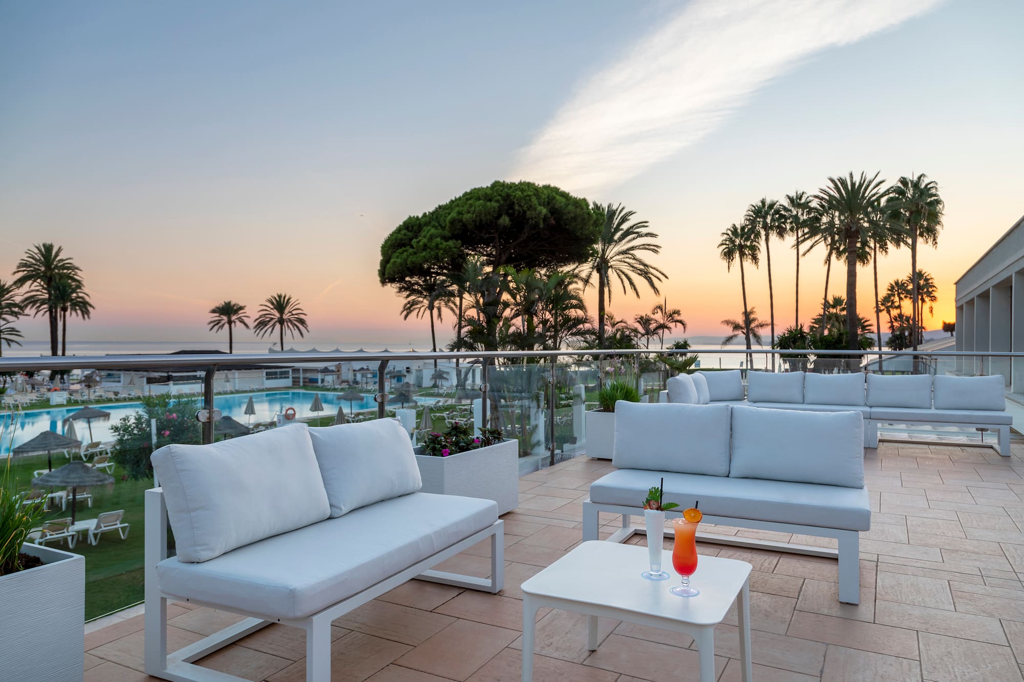 a white couches and tables on a patio with palm trees and a pool