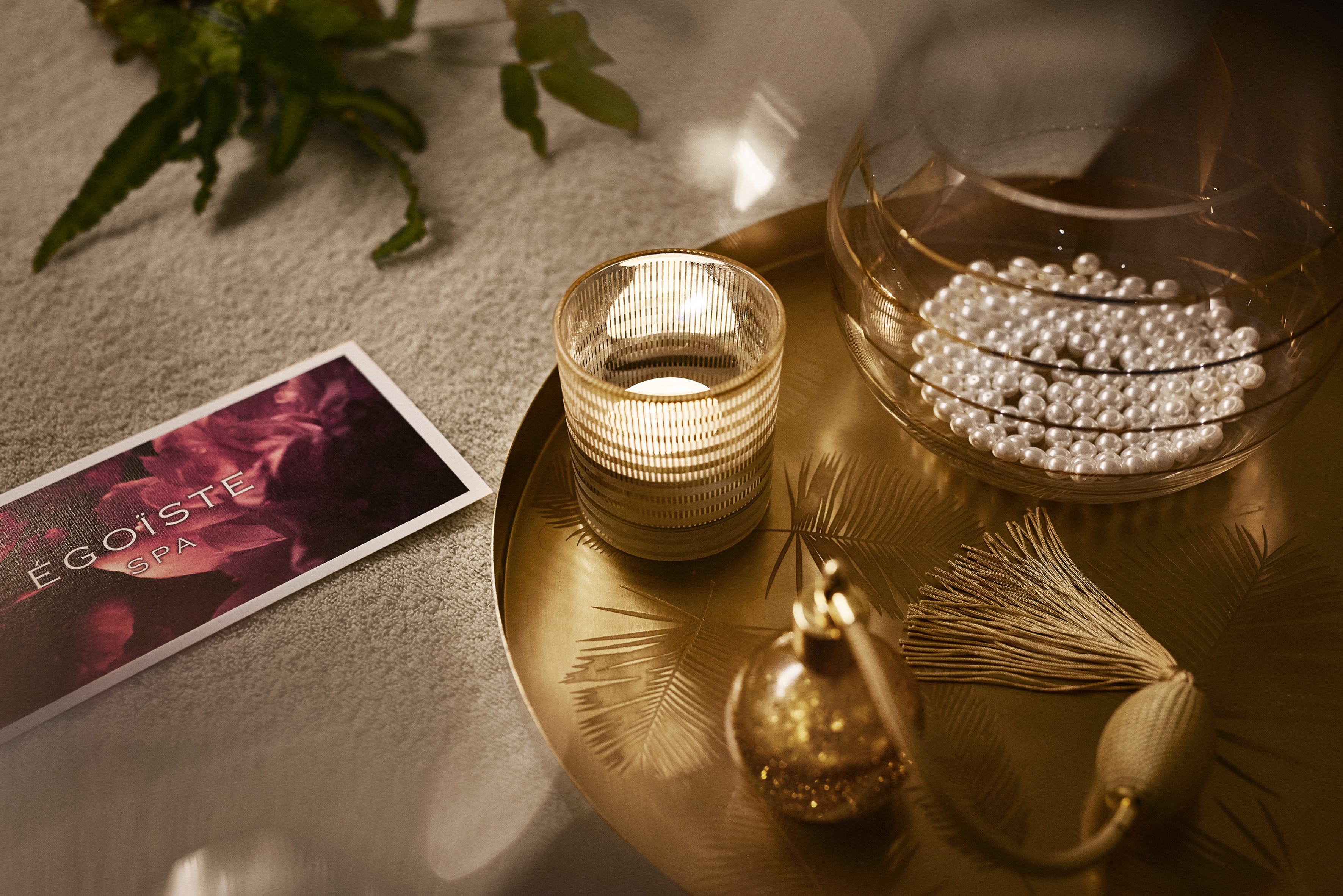 EGOISTE SPA card, lit candle, pearls, and perfume on golden tray. Relaxing ambiance.