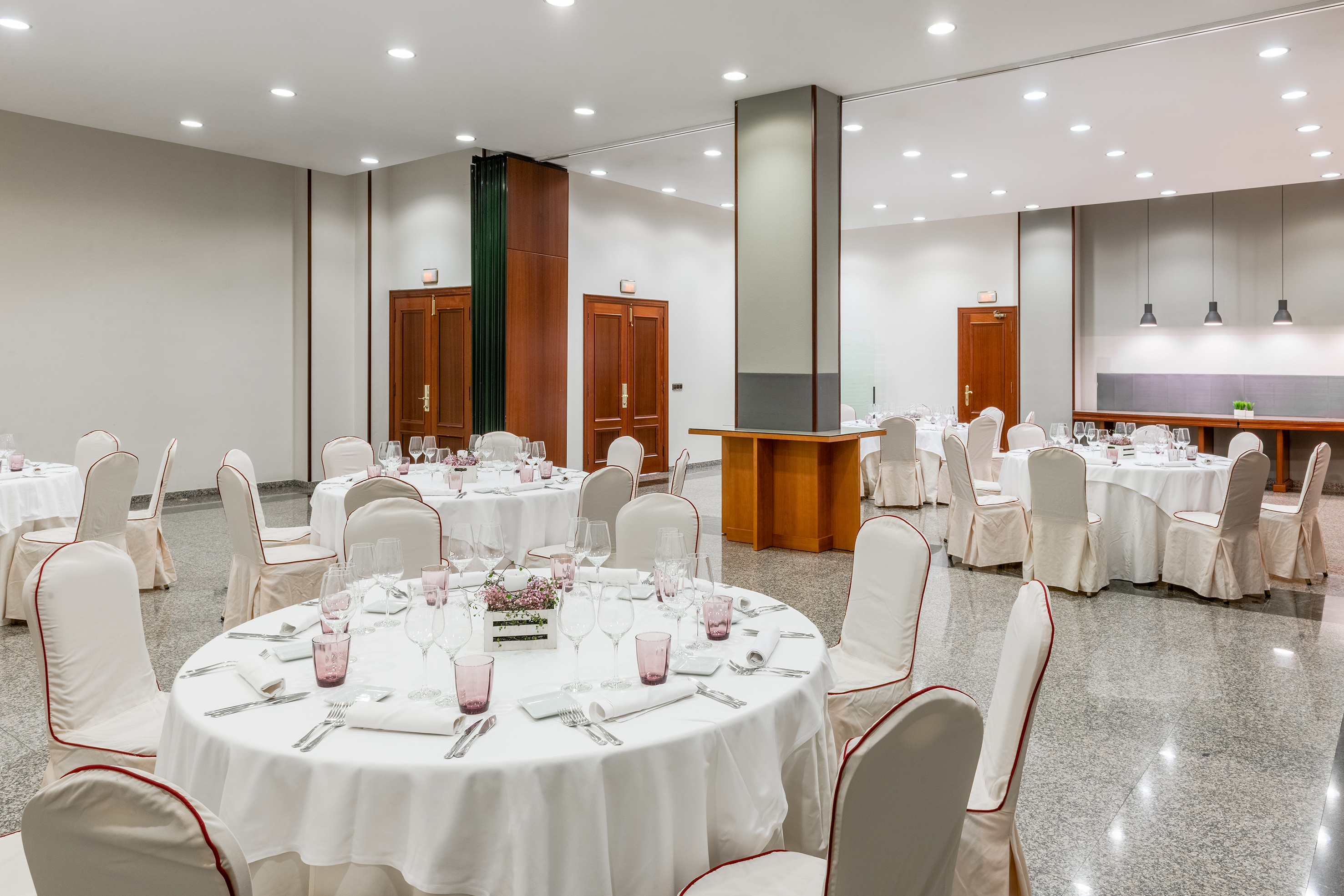 Modern event space with white-linened round tables and covered chairs.