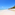White sand beach with turquoise ocean, blue sky, and tropical trees.