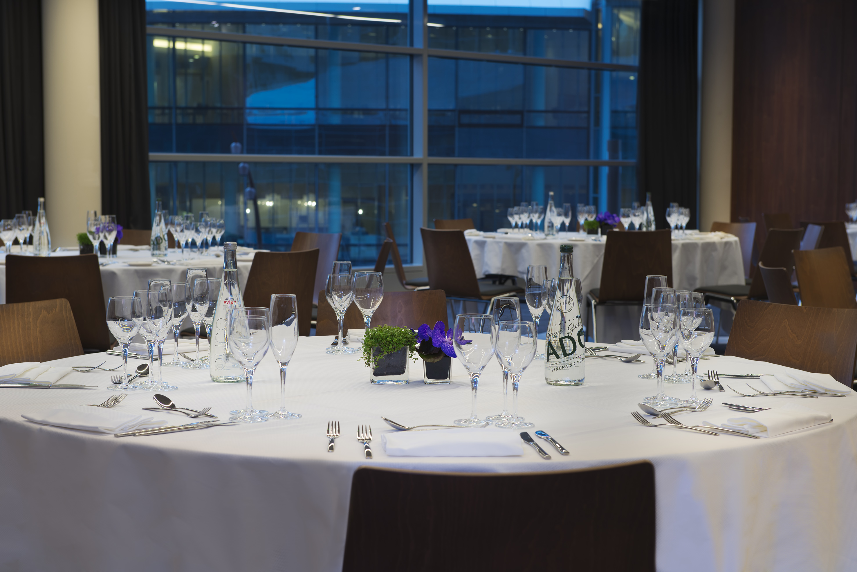 Hotel conference room with set dining tables, chairs, and city window view.