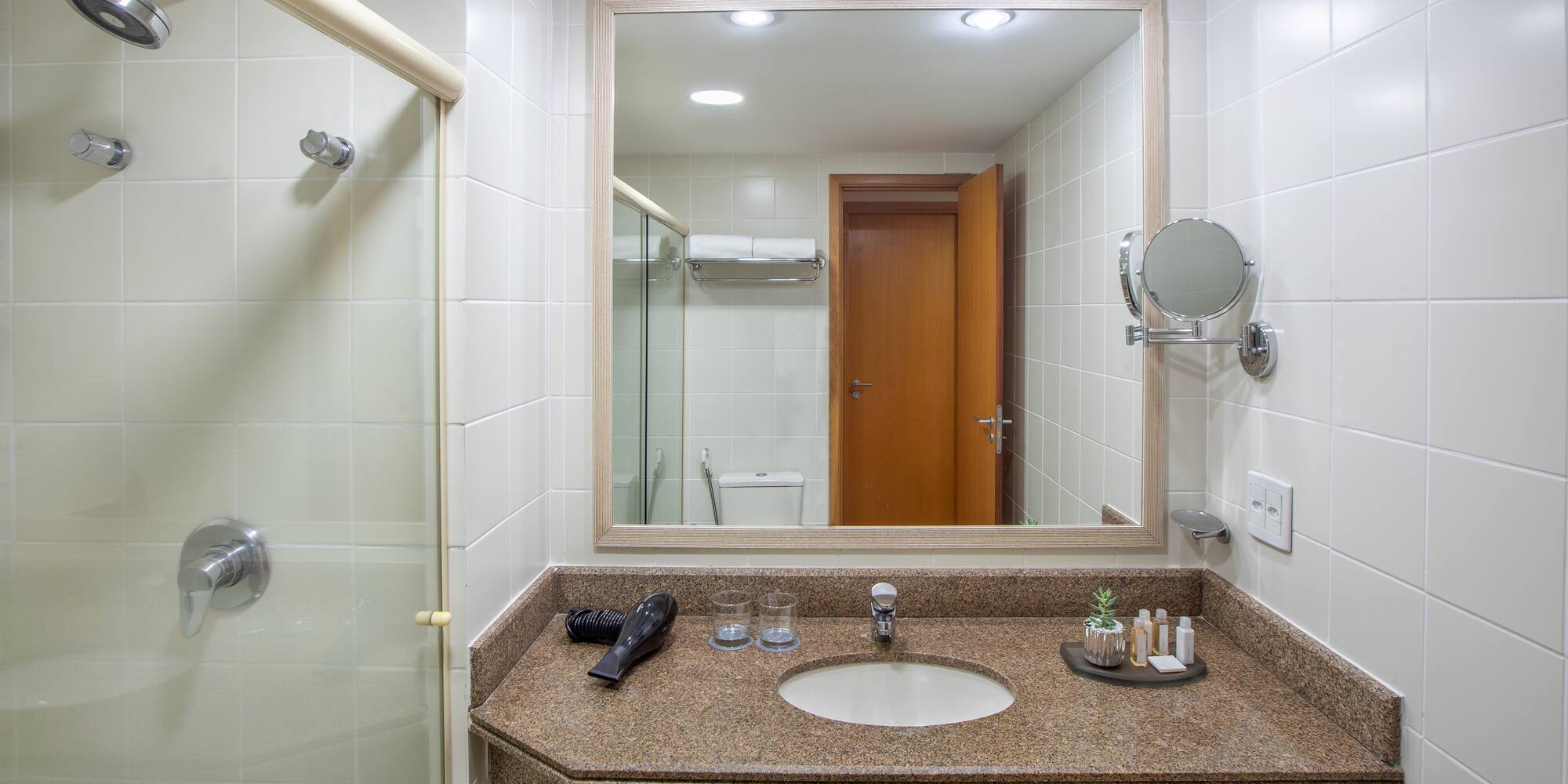 Hotel bathroom with shower, granite vanity, sink, mirror, and guest amenities.
