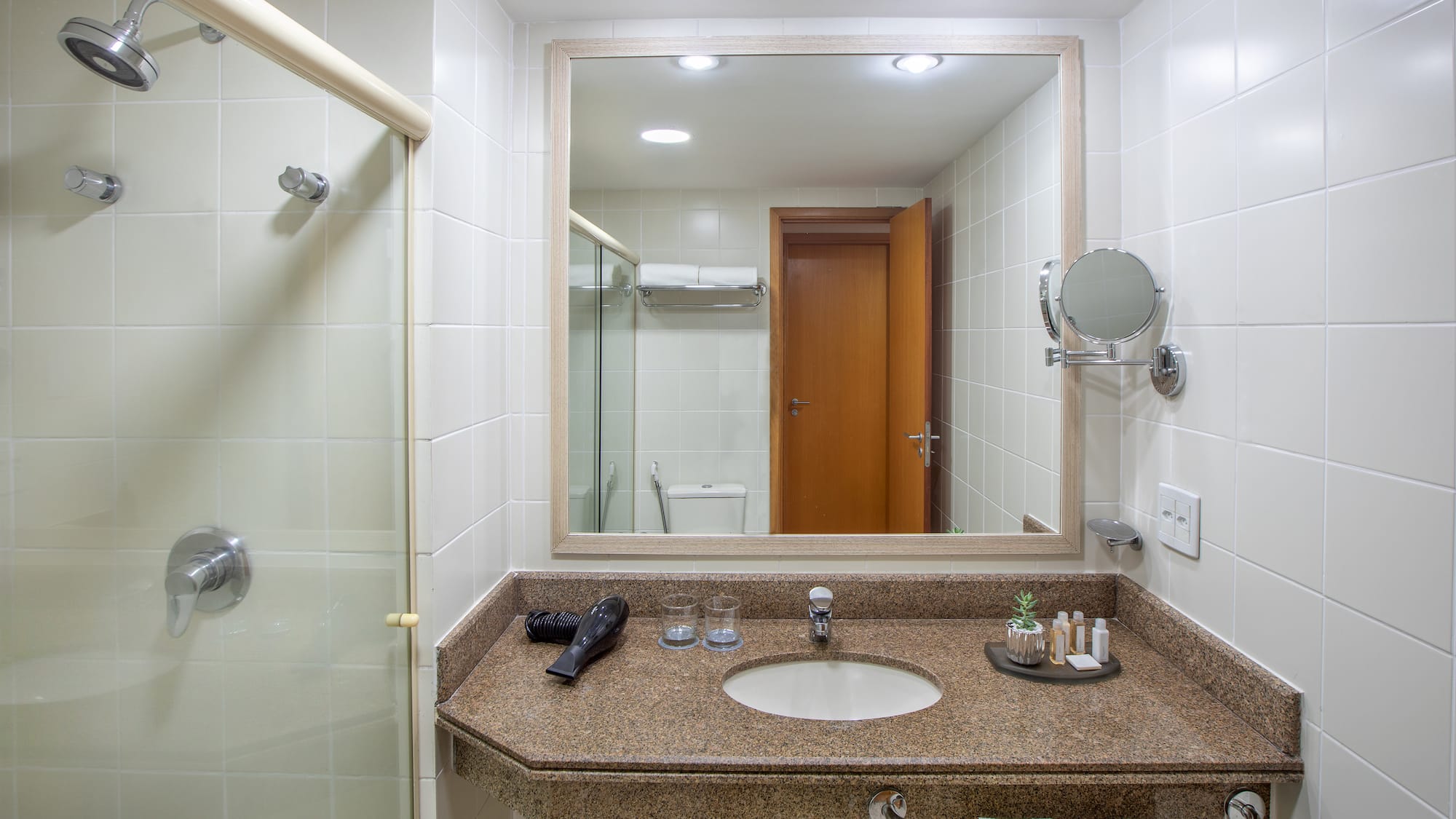 Hotel bathroom with shower, granite vanity, sink, mirror, and guest amenities.
