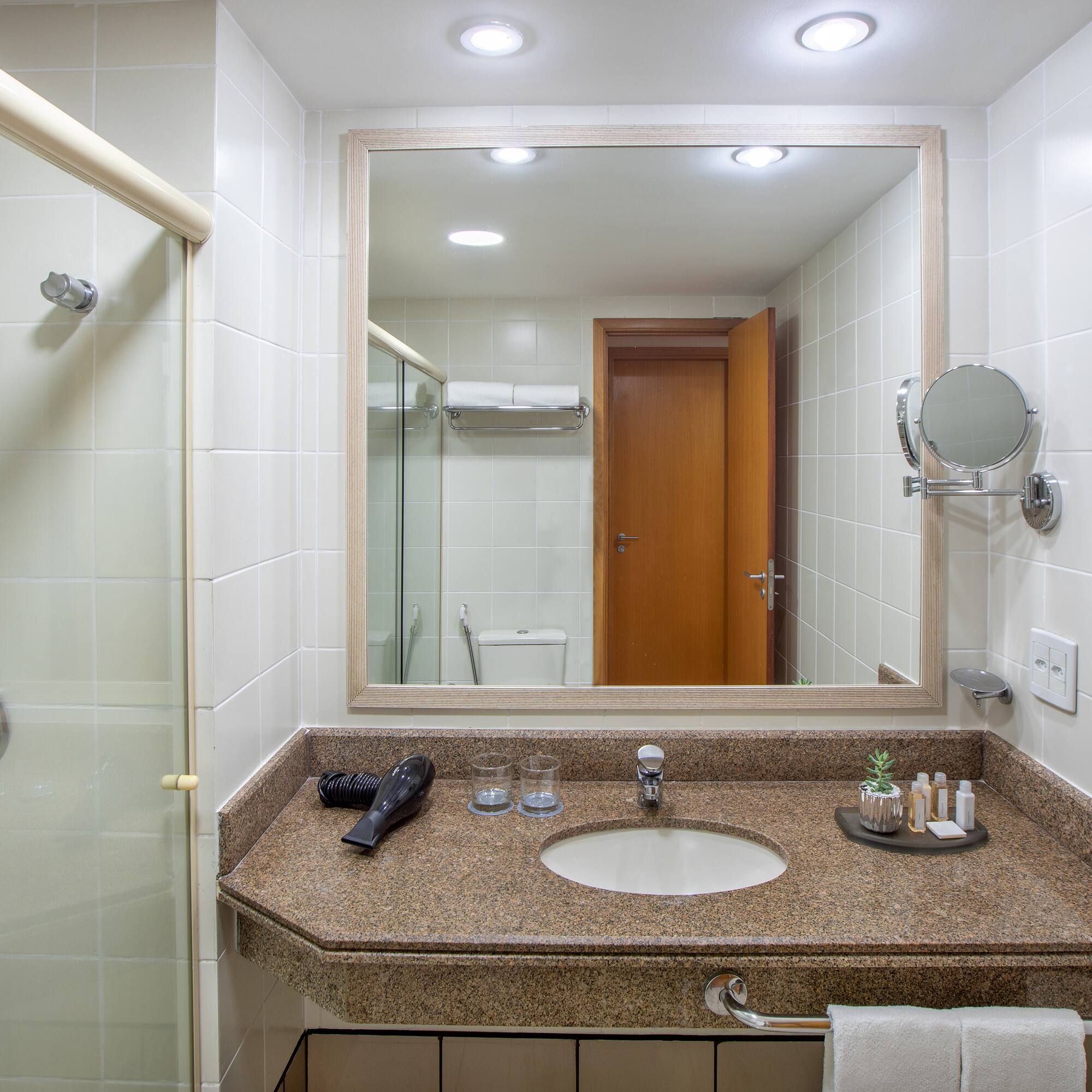Hotel bathroom with shower, granite vanity, sink, mirror, and guest amenities.