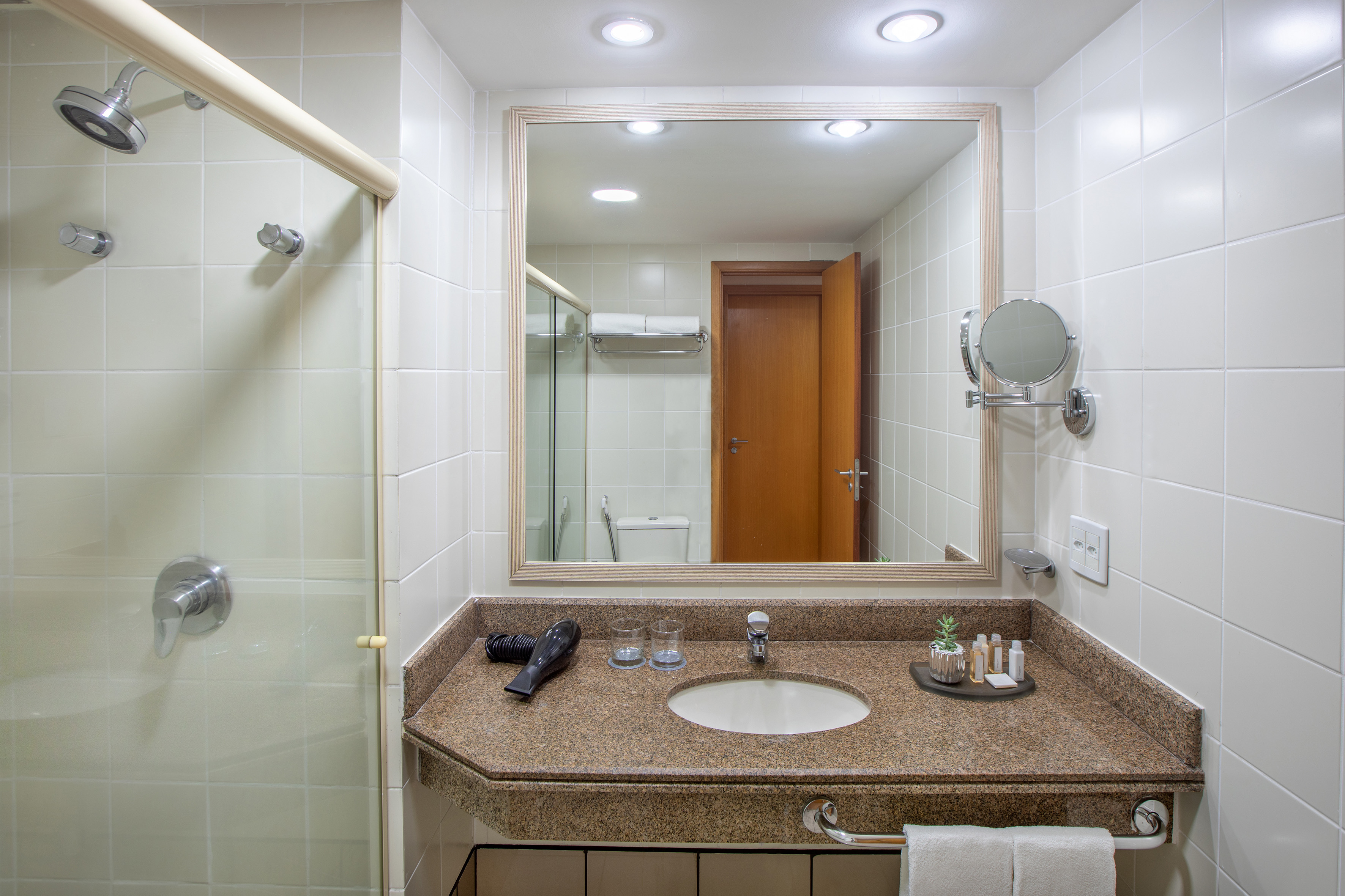Hotel bathroom with shower, granite vanity, sink, mirror, and guest amenities.