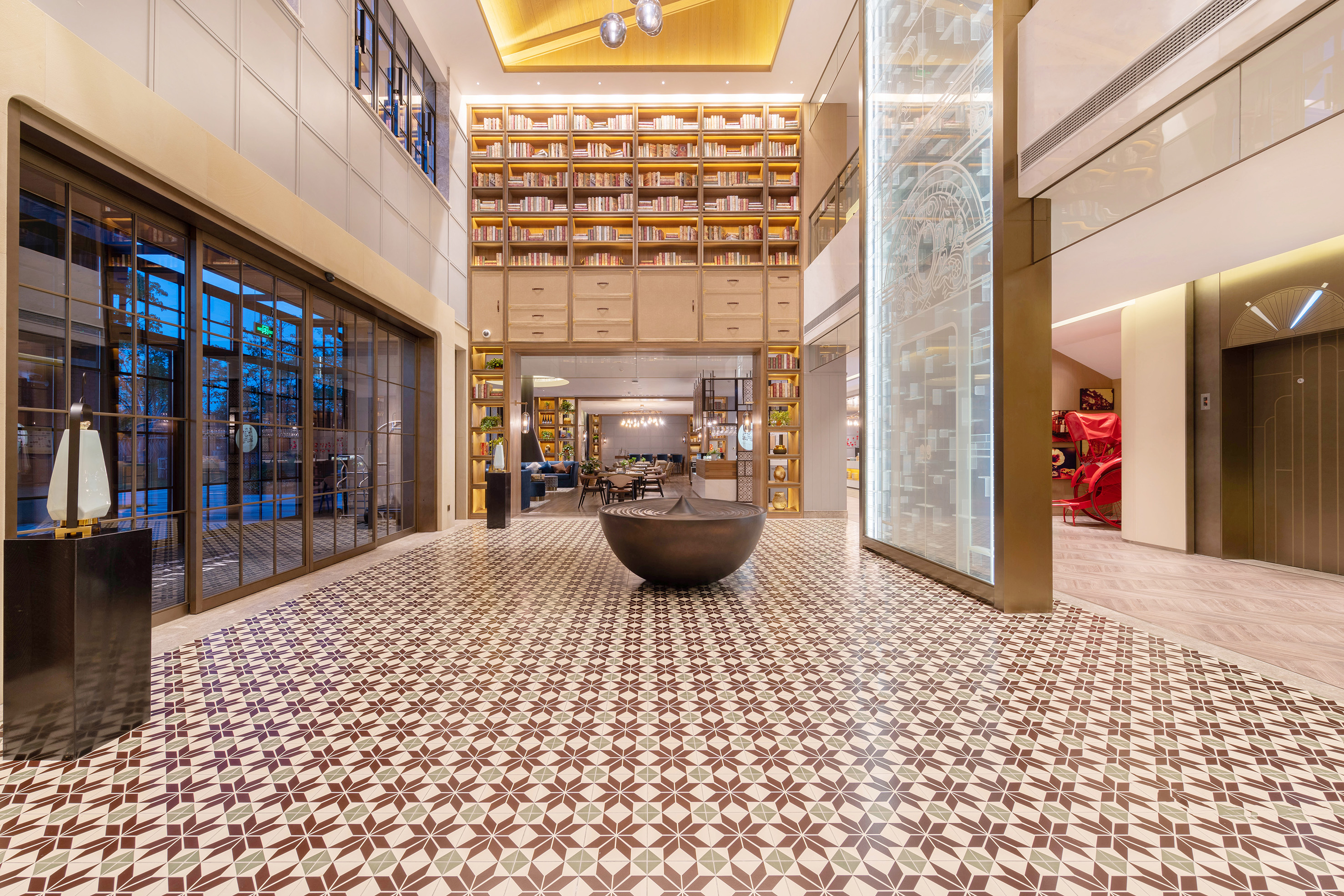 Luxurious hotel lobby with multi-story bookshelf wall and ornate patterned floor.