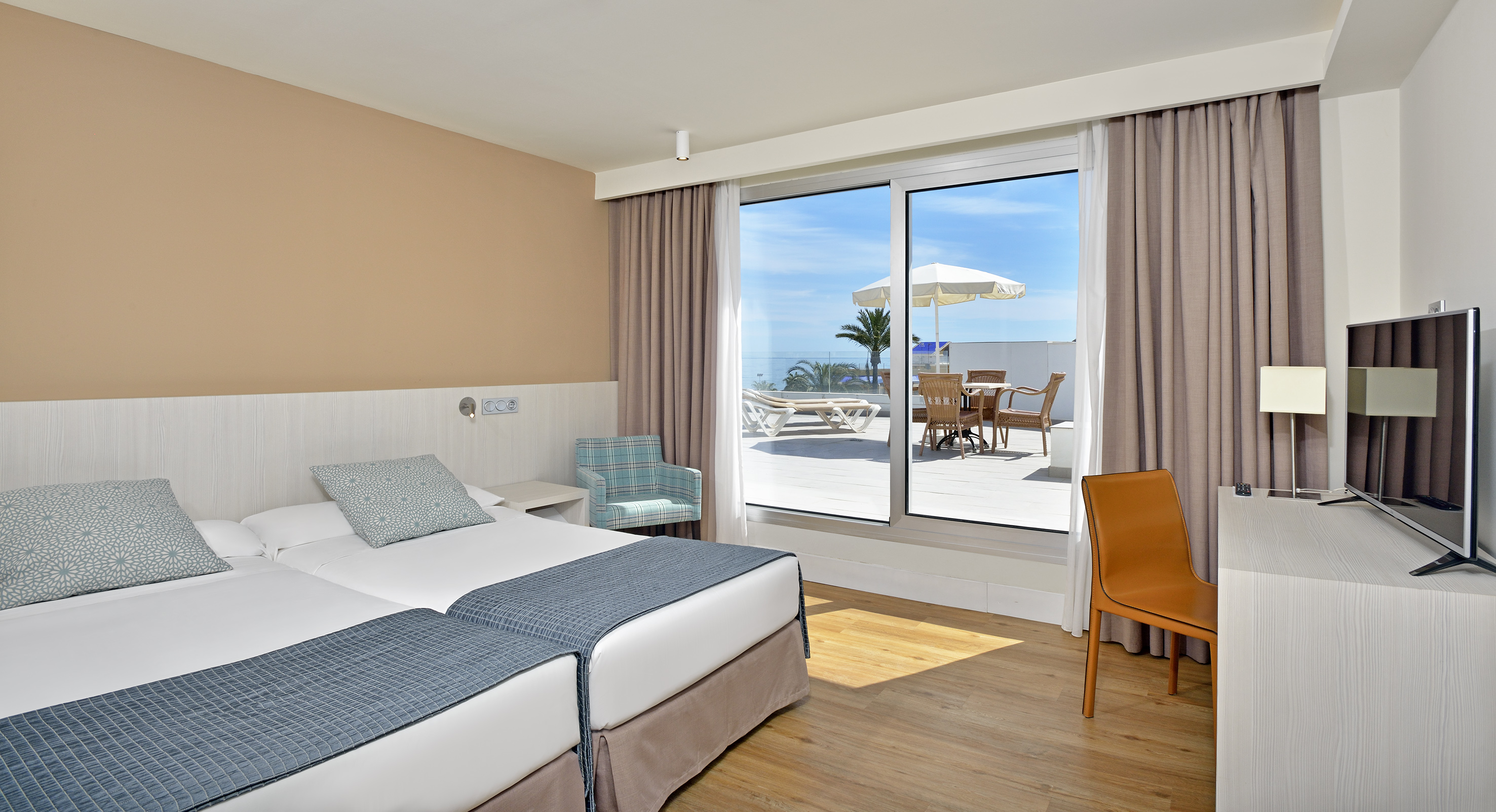 Hotel room with twin beds, balcony, sea view, and outdoor patio set.