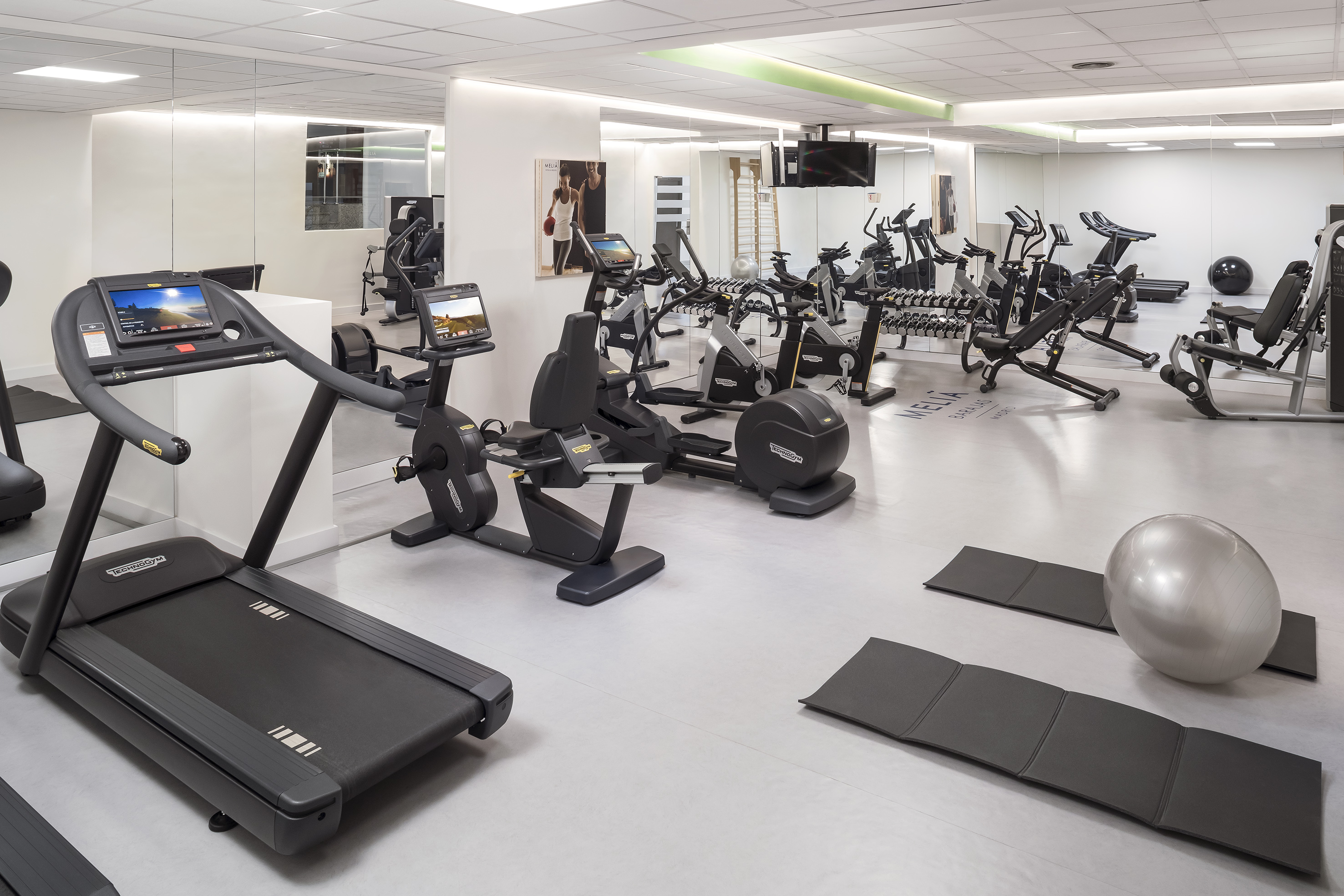 Modern Meliá hotel gym with Technogym equipment: treadmill, bikes, and weights.