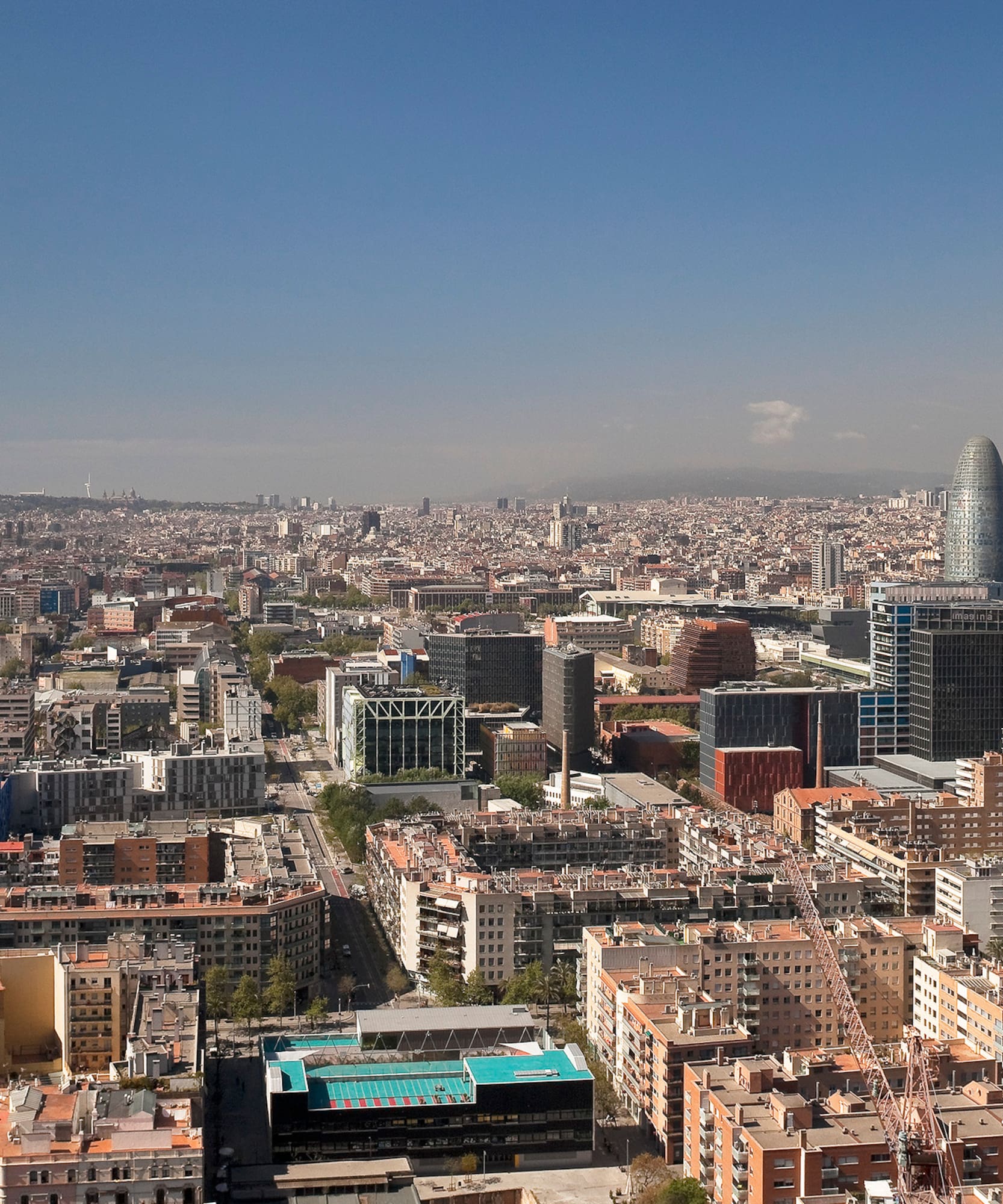 Vista aérea de Barcelona con Torre Glòries, Sagrada Familia y Montjuïc bajo cielo azul.