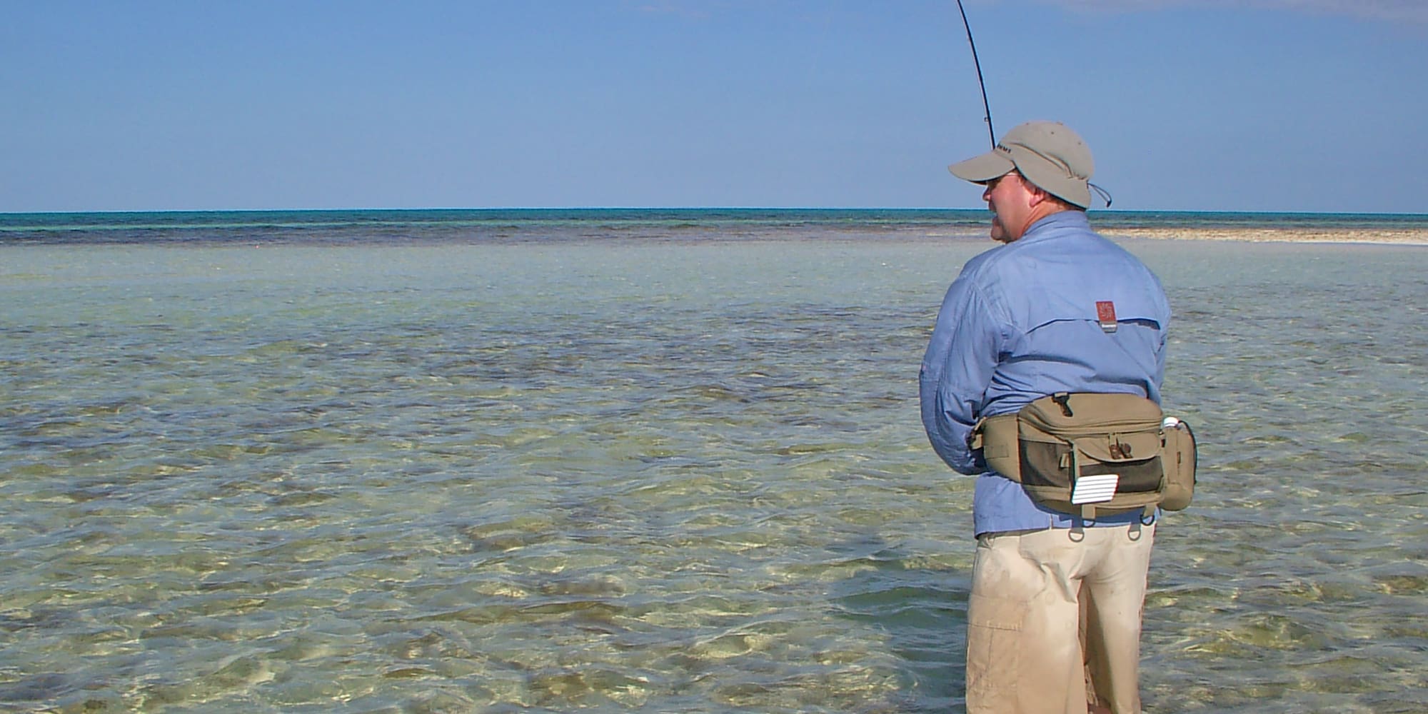 a man standing in shallow water holding a fishing pole